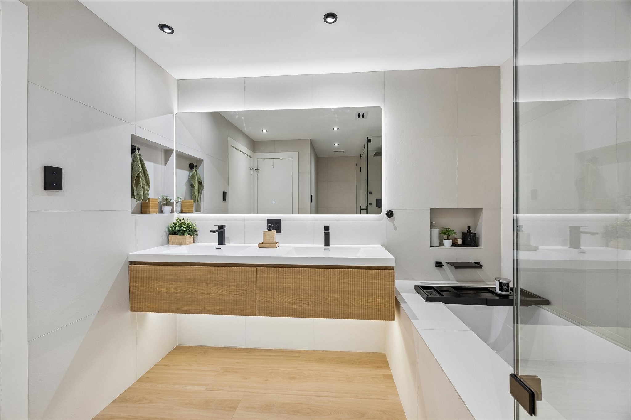 Floating double vanity provides two sinks and drawer storage beneath a wide illuminated mirror.
