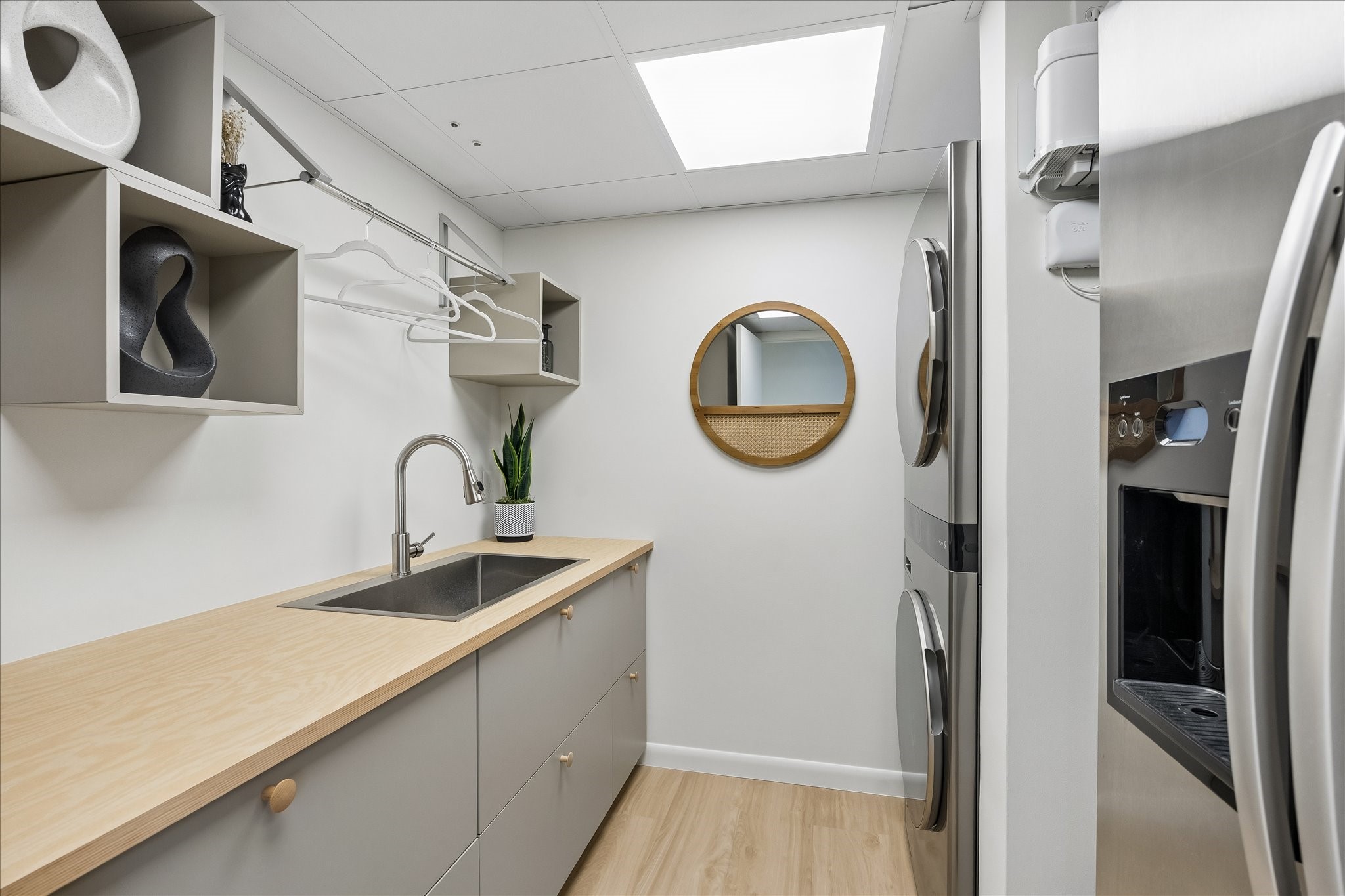 Utility room combines a sink, long countertop, cabinetry and hanging space beside stacked LG washer/dryer appliances with remote app control. An extra side-by-side refrigerator provides additional cold storage.