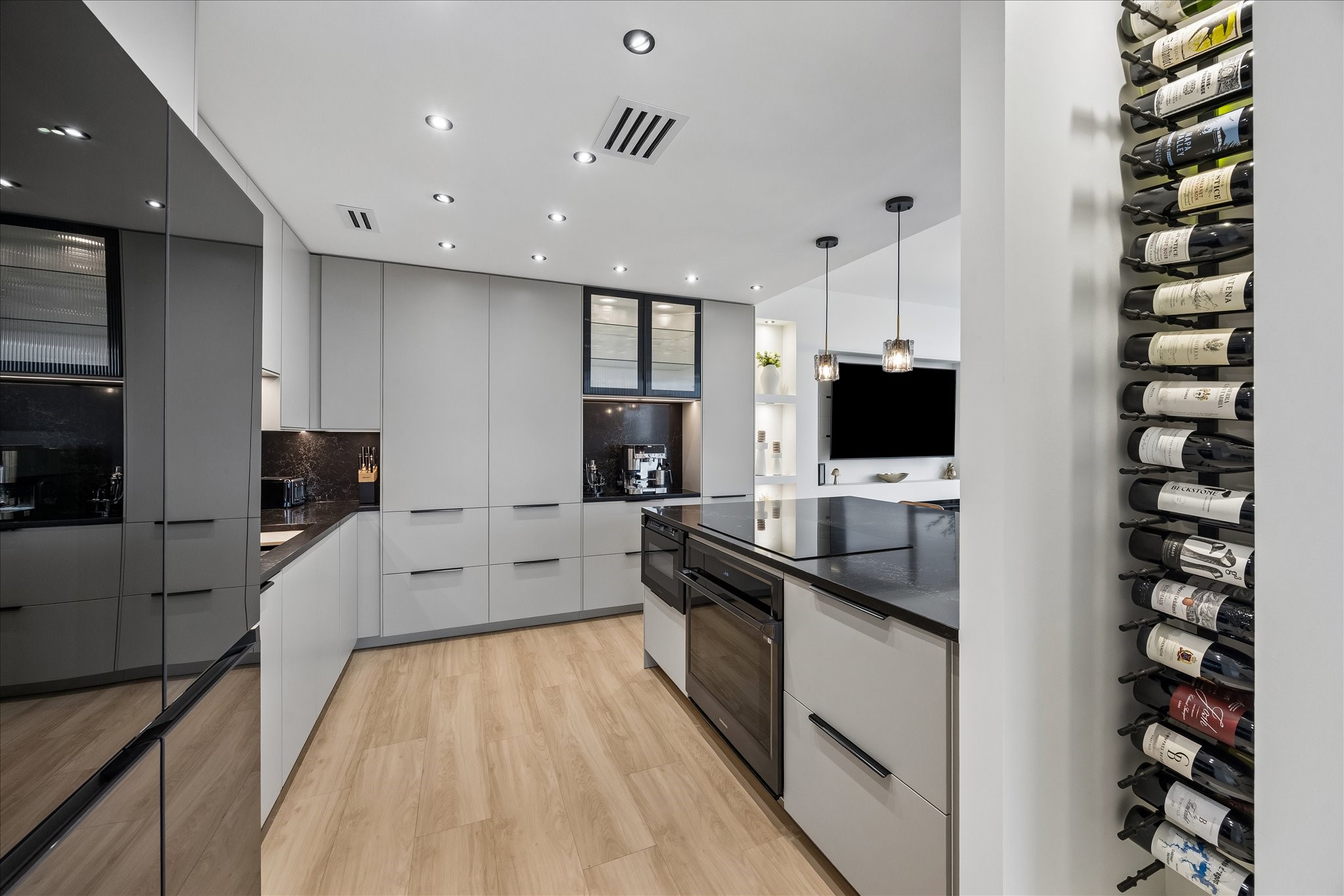 Tall cabinetry and glass front uppers provide storage beside a wall mounted wine display.