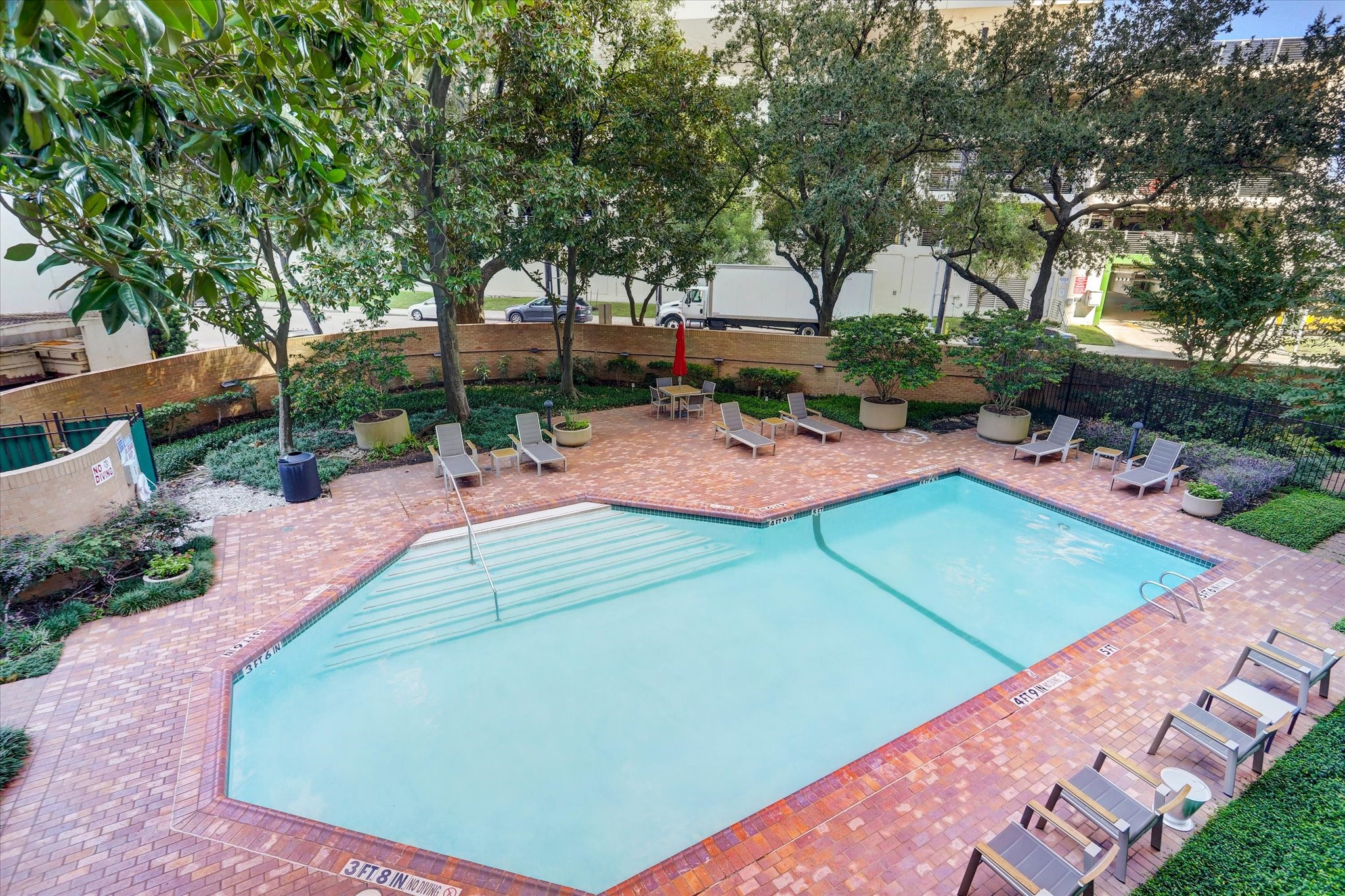 A landscaped courtyard with a heated, temperature-controlled pool offers a relaxing outdoor escape, with a spacious brick terrace, poolside lounge seating and mature trees framing the setting.