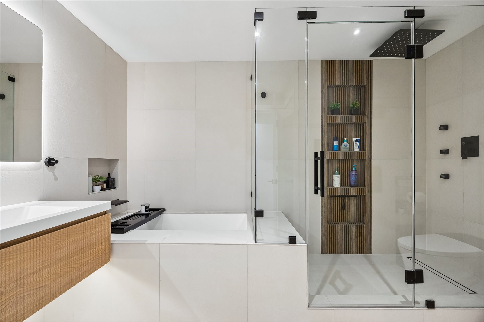 Separate bathtub and glass enclosed shower offer distinct bathing spaces, with recessed storage within reach.