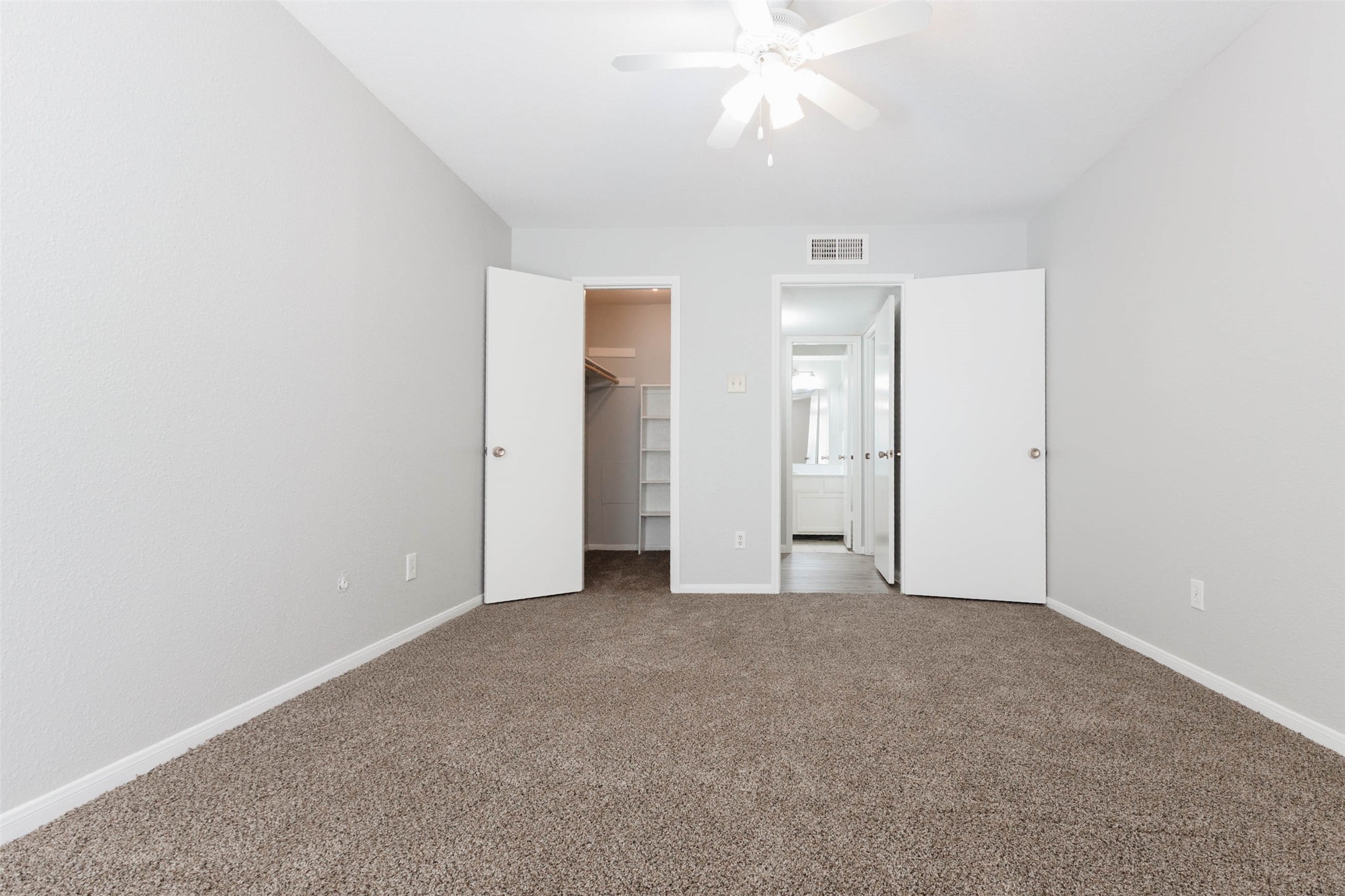 Large carpeted bedroom with ceiling fan, neutral walls, and double-door closet access.