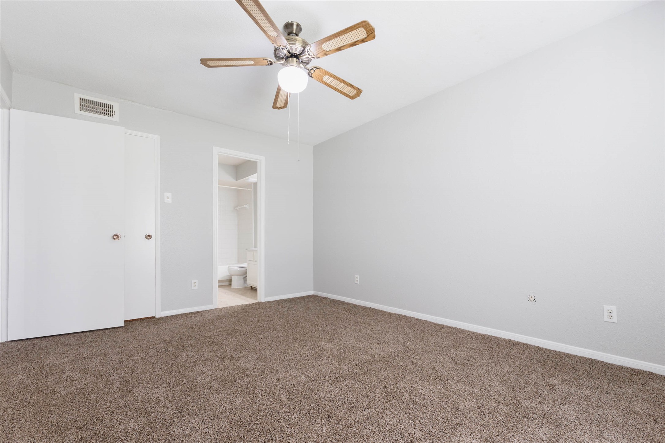 Spacious carpeted bedroom featuring neutral paint, ceiling fan, and convenient access to the adjoining bathroom.