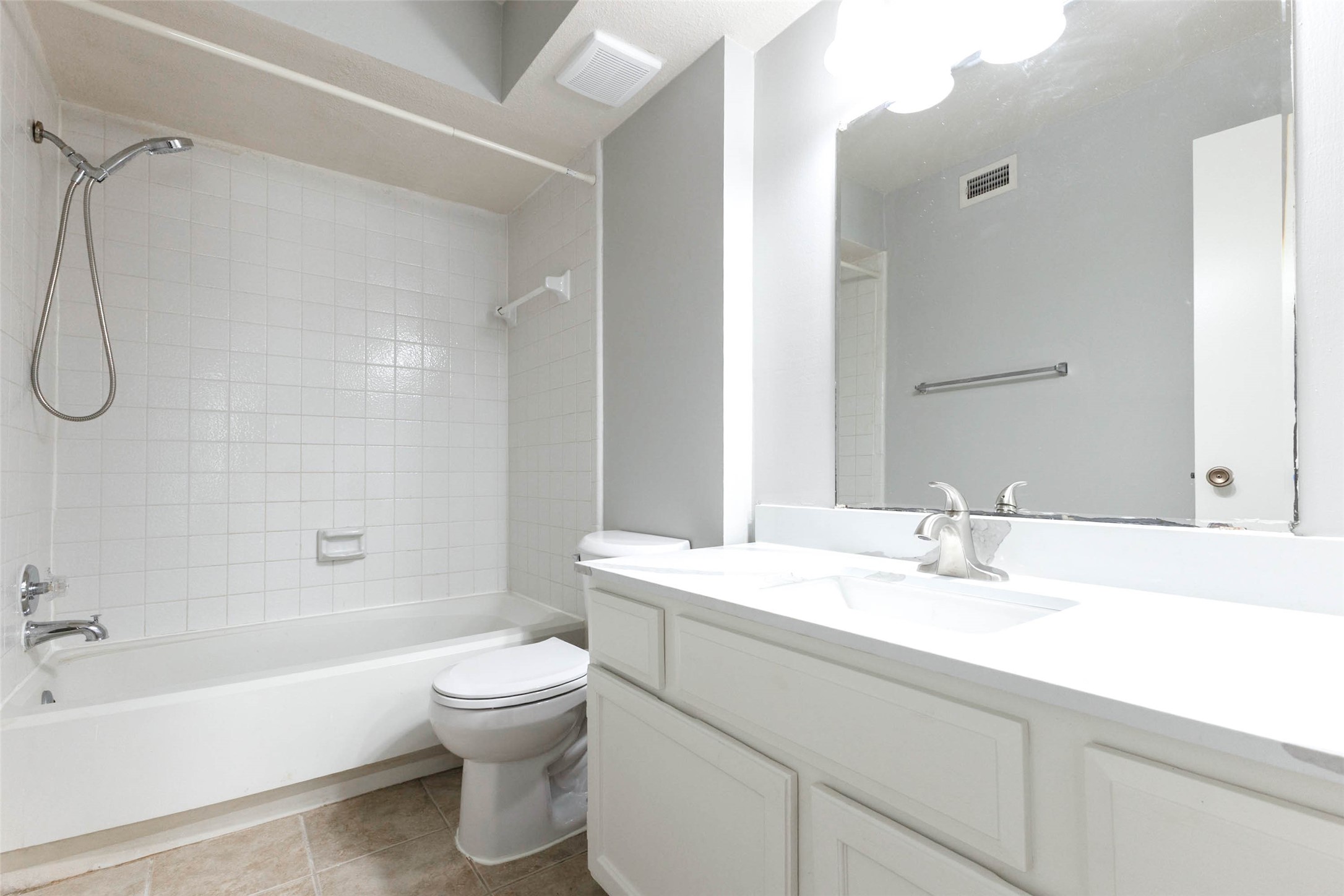 Full bathroom featuring a spacious vanity with countertop storage, large mirror, and tub/shower combination.