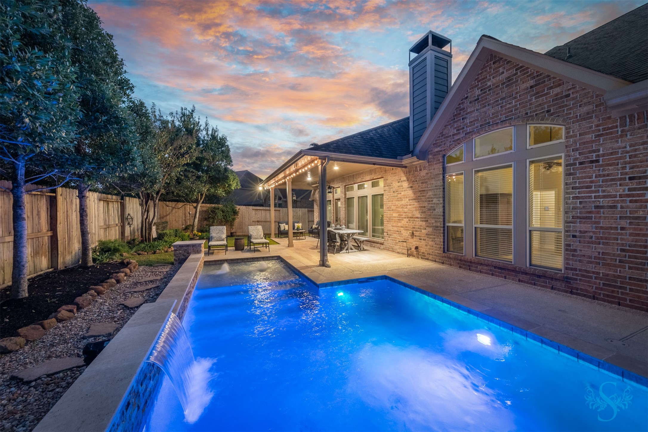 Brilliant blue pool lighting and a cascading waterfall transform the backyard into an enchanting evening escape. Enjoy a refreshing swim before unwinding beneath the covered patio, surrounded by lush landscaping and the soothing sound of water. Brilliant blue pool lighting and a cascading waterfall transform the backyard into an enchanting evening escape. Enjoy a refreshing swim before unwinding beneath the covered patio, surrounded by lush landscaping and the soothing sound of water.