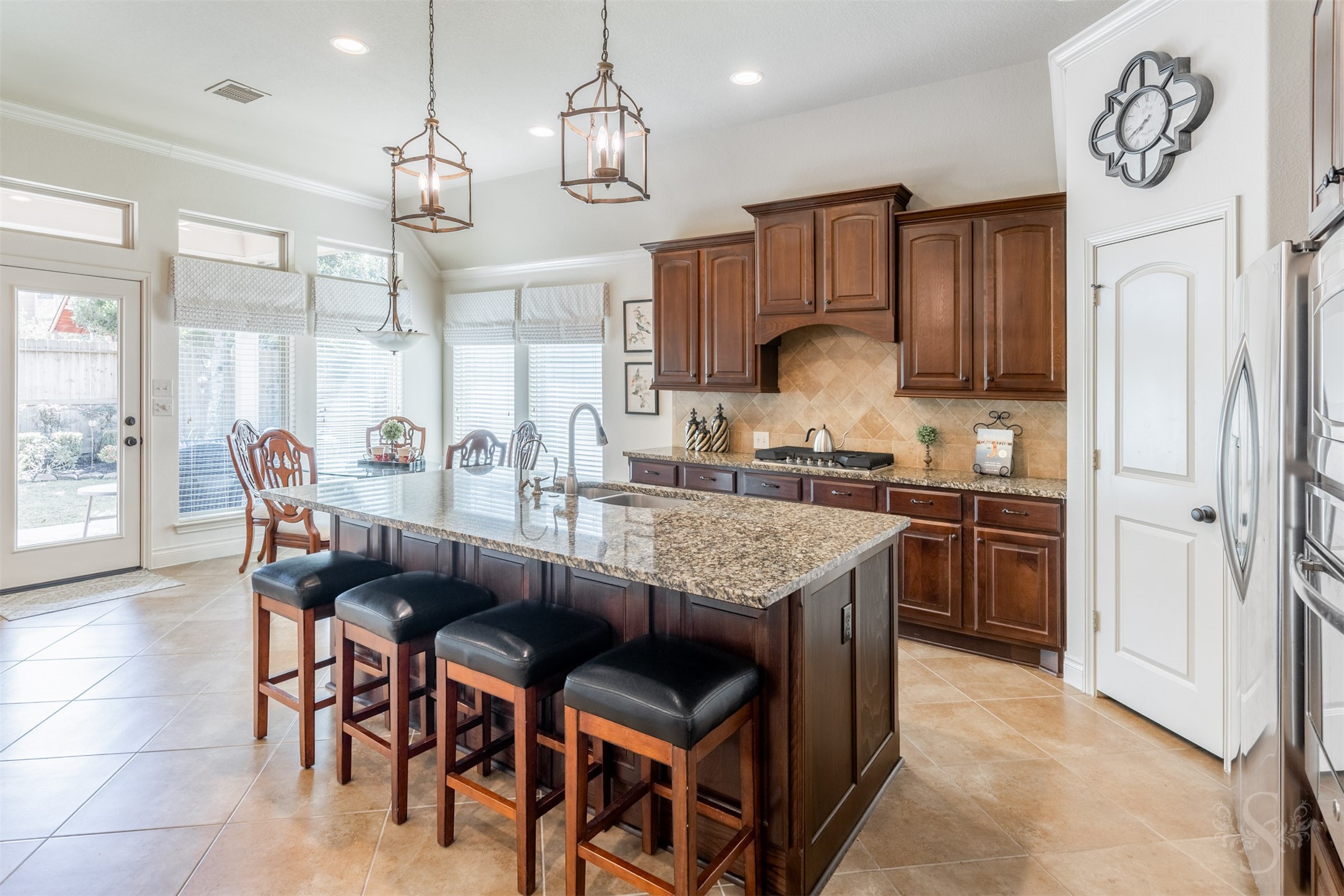The beautifully appointed kitchen pairs an expansive granite island with rich raised panel cabinetry and a gas cooktop. Breakfast bar seating and the adjoining breakfast room offer inviting places to gather, with tall windows framing views of the backyard.