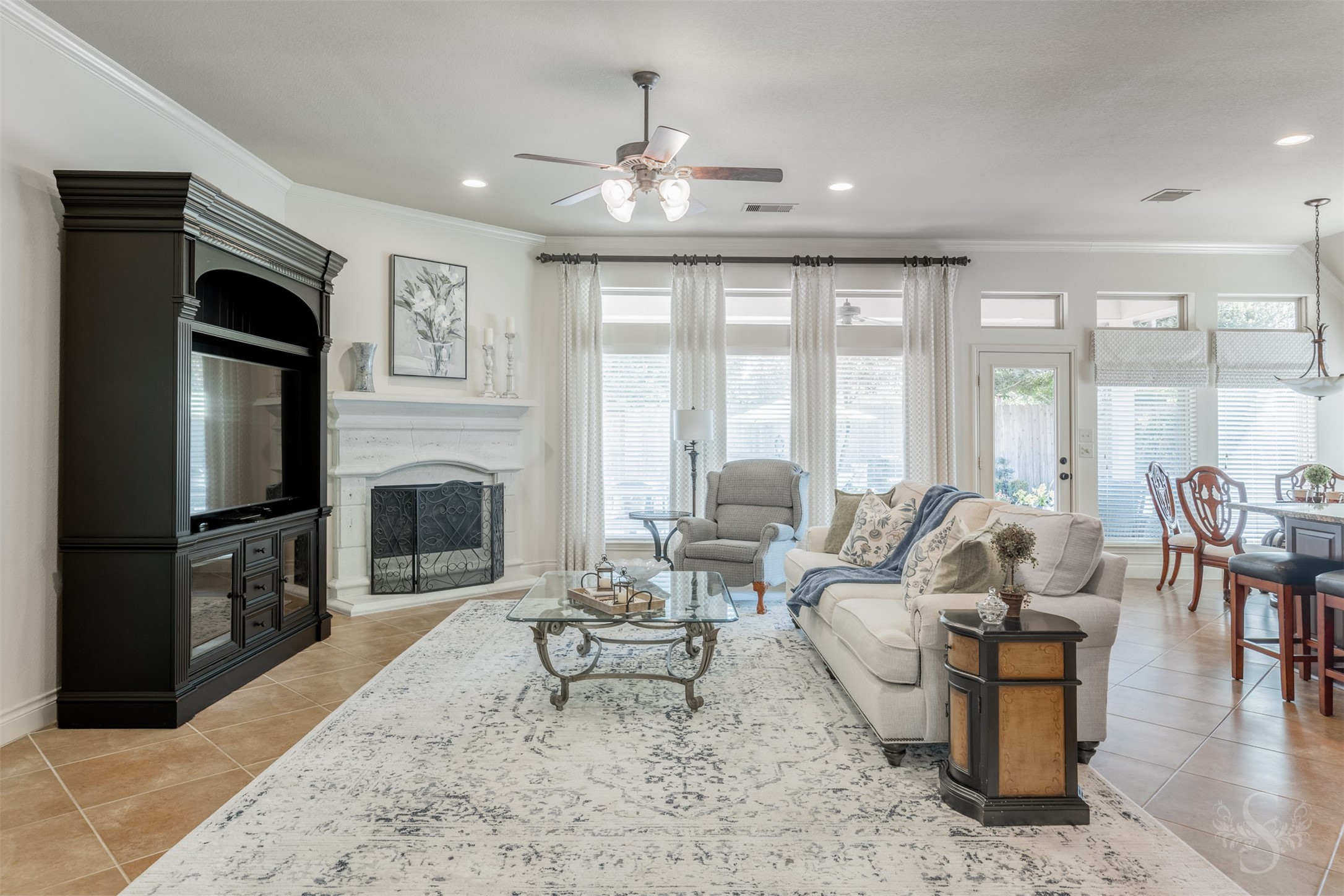 A beautifully detailed cast-stone fireplace creates an elegant focal point in the spacious family room, offering a cozy setting for relaxed evenings. Tall windows topped by transoms span the back wall, while a glass door provides convenient access to the extended covered patio.