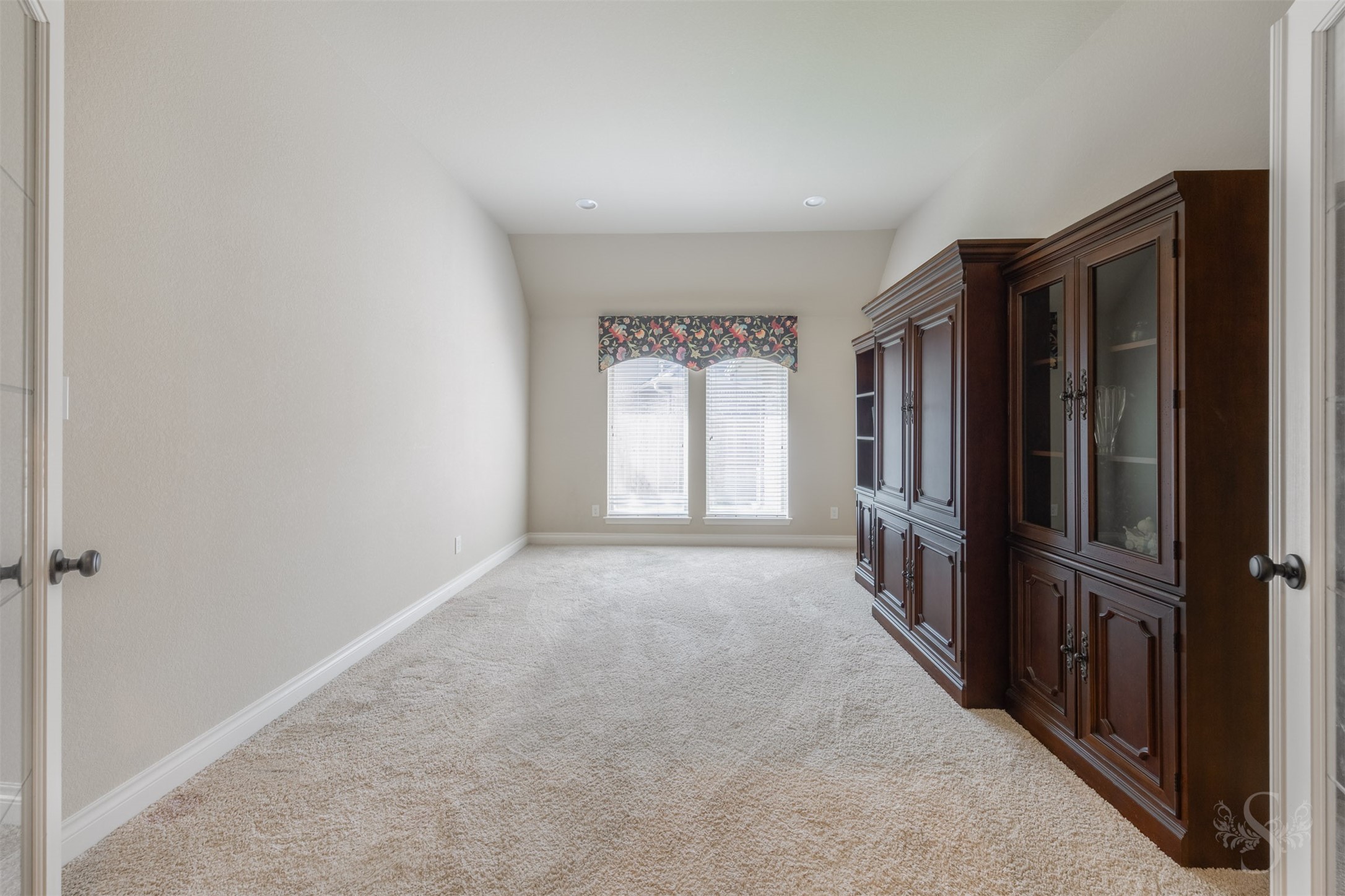 Glass double doors open to a spacious flex room with soft carpeting, recessed lighting and tall windows that brighten the inviting interior. This versatile space offers endless possibilities for a comfortable sitting room, creative studio or favorite hobbies.