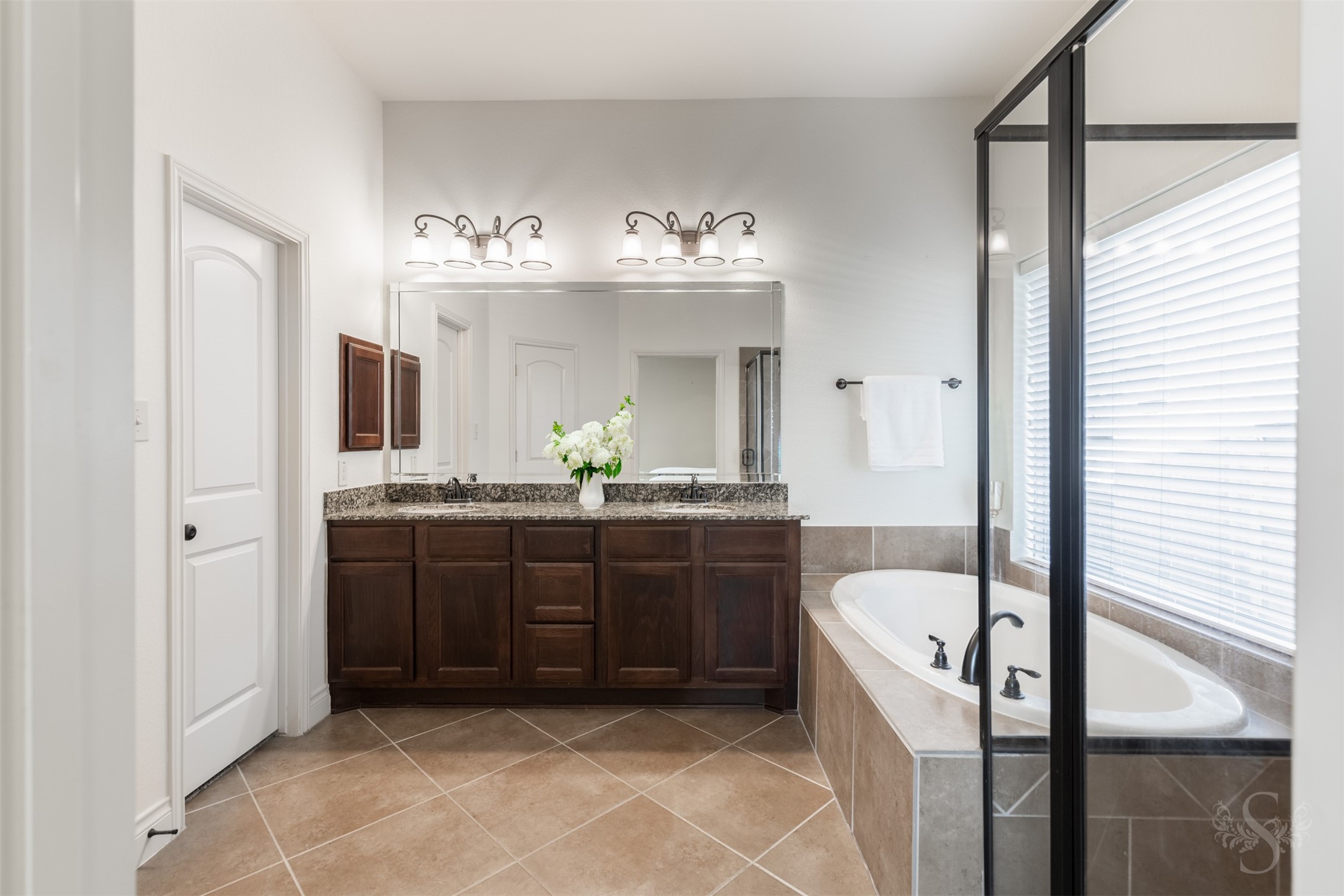 The spacious primary bath pairs a granite vanity with dual sinks and rich cabinetry for an elegant start to your daily routine. A garden tub and separate glass-enclosed shower offer inviting options for relaxation and refreshment.