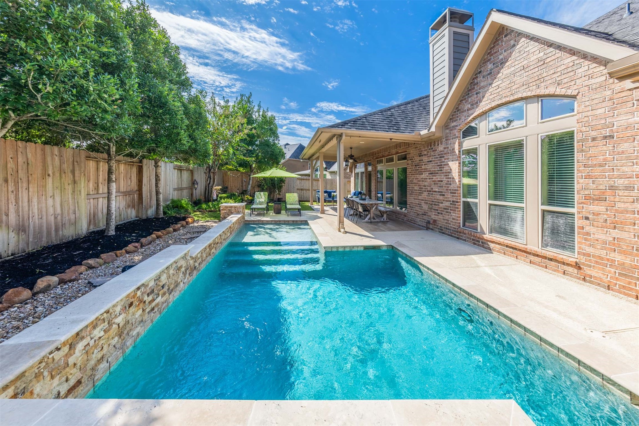 Spend sun-filled afternoons swimming and relaxing in the sparkling pool, beautifully framed by a raised stone wall and lush landscaping. The covered patio offers a welcoming place for poolside dining and leisurely conversation in this exquisite backyard retreat.