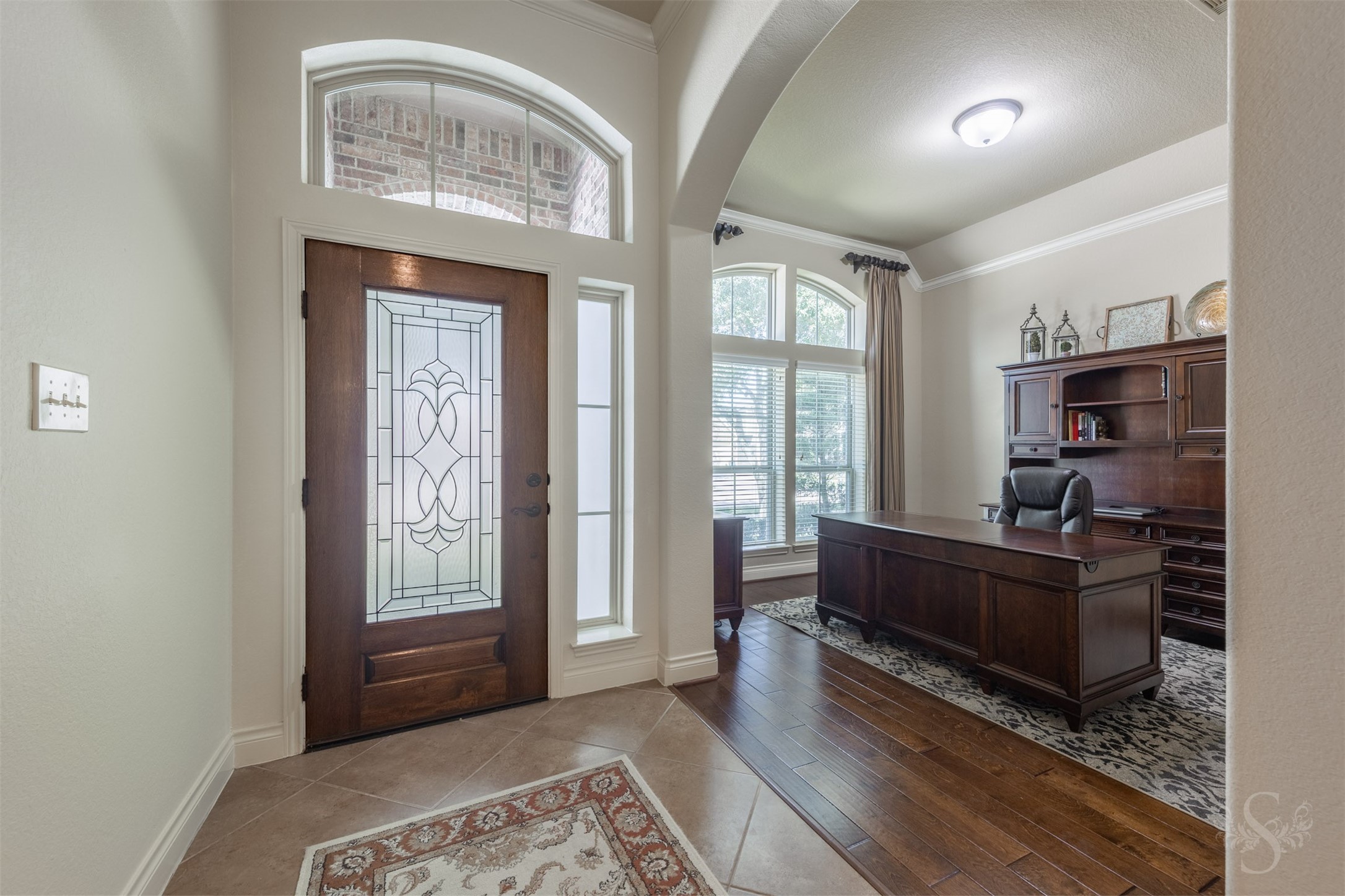A decorative glass front door and arched transom introduce an elegant entry accented by diagonal tile flooring. Just off the entry, a graceful archway opens to the study, where rich wood flooring and an expansive front window create a warm, inviting workspace.