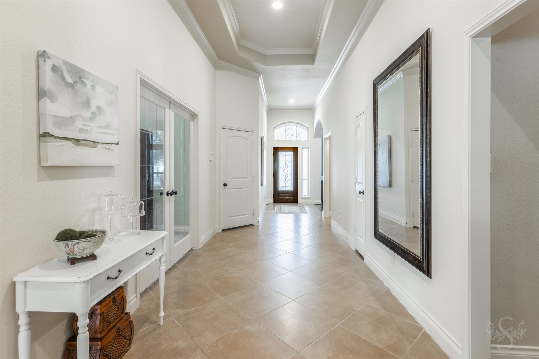 An impressive tray ceiling edged in crown molding draws the eye along the extended entry, showcasing the homes exquisite architectural detail. Diagonally laid tile and graceful arched openings create an elegant passage toward the main gathering spaces.