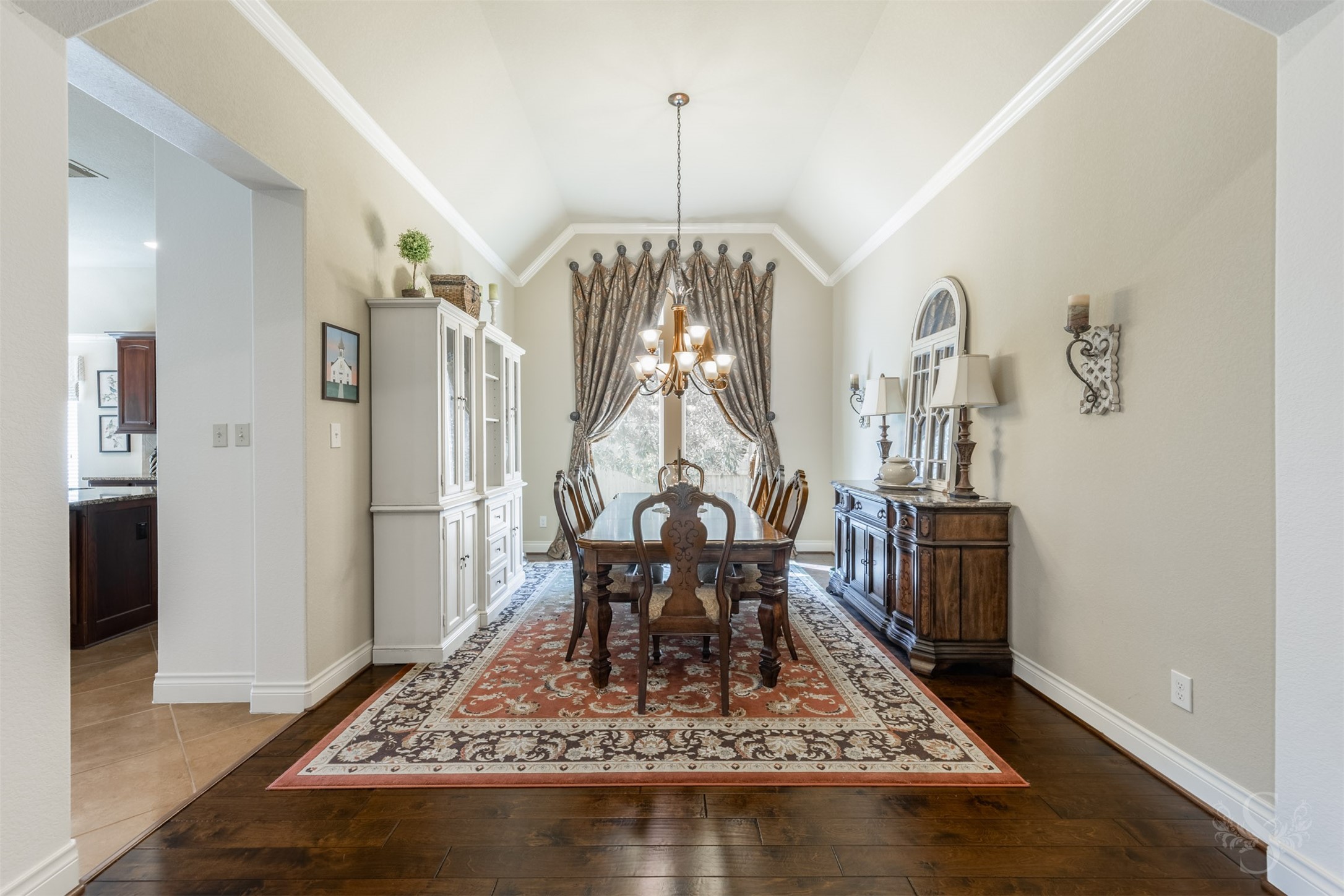 Rich wood flooring and a lofty ceiling outlined in crown molding create an elegant setting in the formal dining room. A graceful chandelier and tall window enhance this inviting space for memorable dinners and entertaining friends.