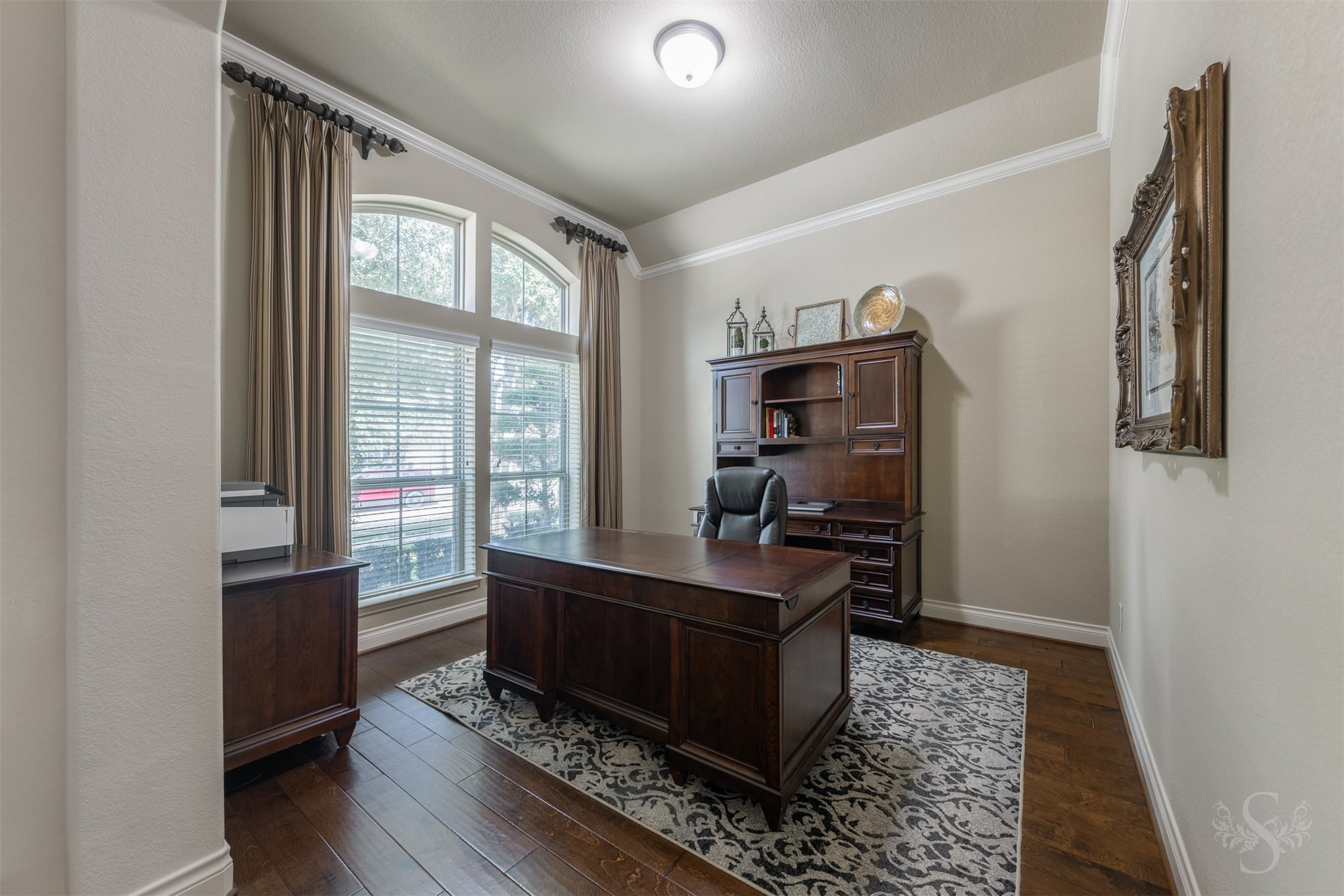 Rich wood flooring and crown molding lend timeless elegance to the study, conveniently located just off the entry. A stunning arched window frames views of the landscaped front yard, creating a beautiful setting for working from home or enjoying a quiet read.