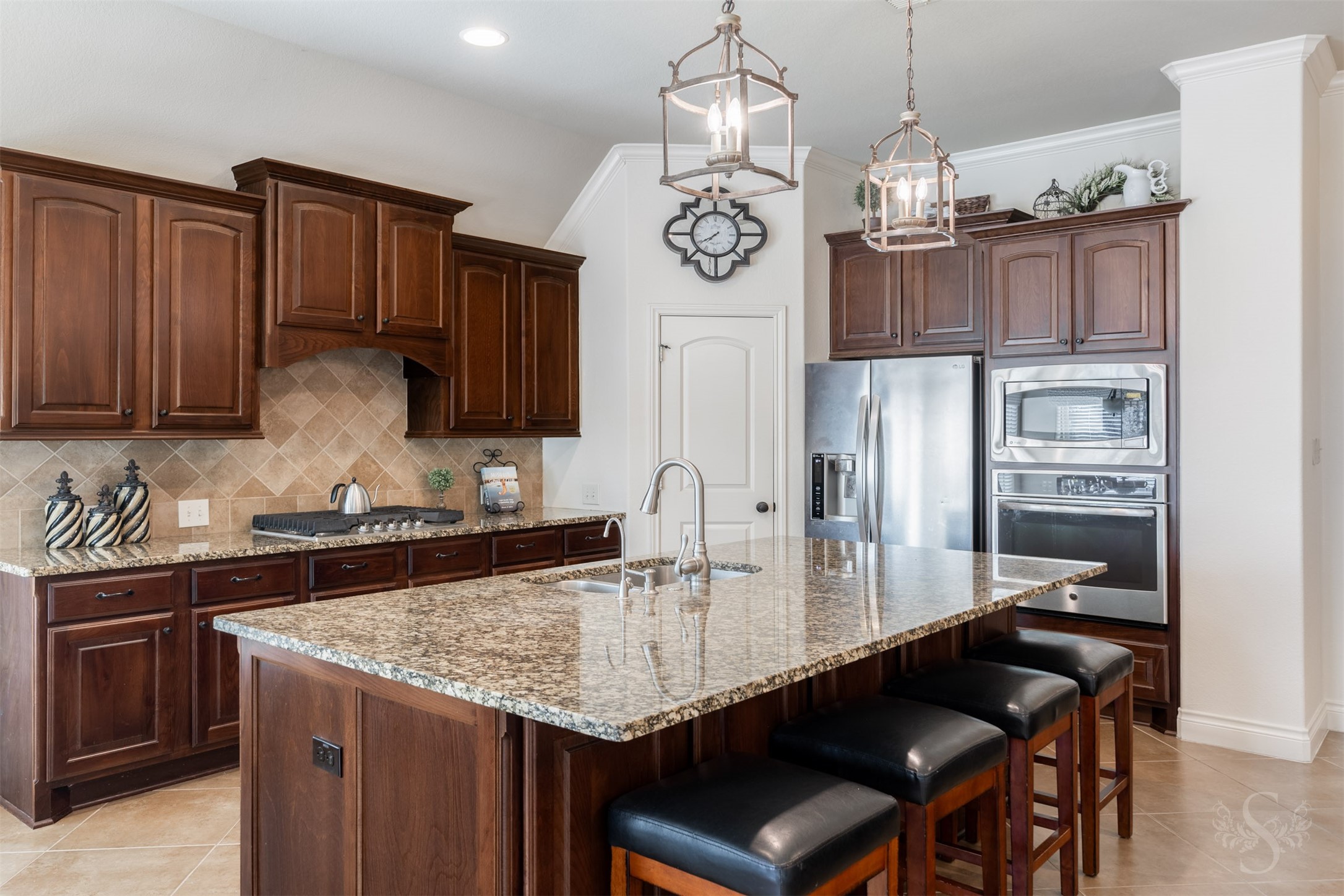 An expansive granite island with breakfast bar seating takes center stage beneath a pair of elegant lantern pendants. Richly stained 42-inch raised panel cabinetry, a diagonal tile backsplash and built-in stainless steel oven and microwave give the kitchen its timeless appeal.
