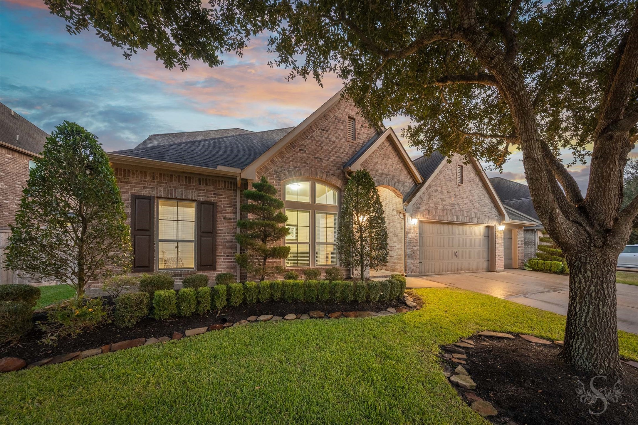 Warm evening illumination highlights the intricate brickwork, graceful gables and impressive arched entrance. Sculpted topiaries and beautifully bordered landscaping complement the homes timeless elegance.