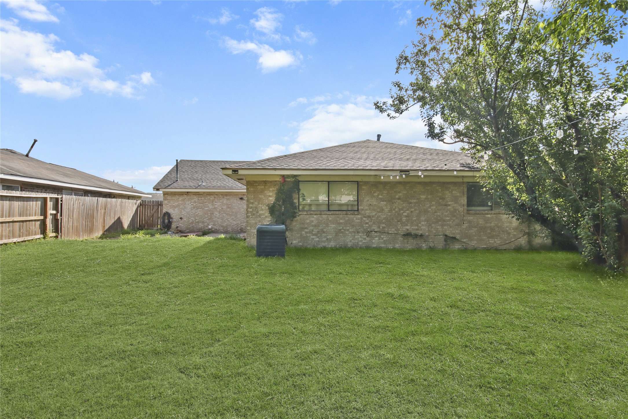 A large grassy backyard provides plenty of room to relax or entertain, framed by mature trees and a privacy fence.