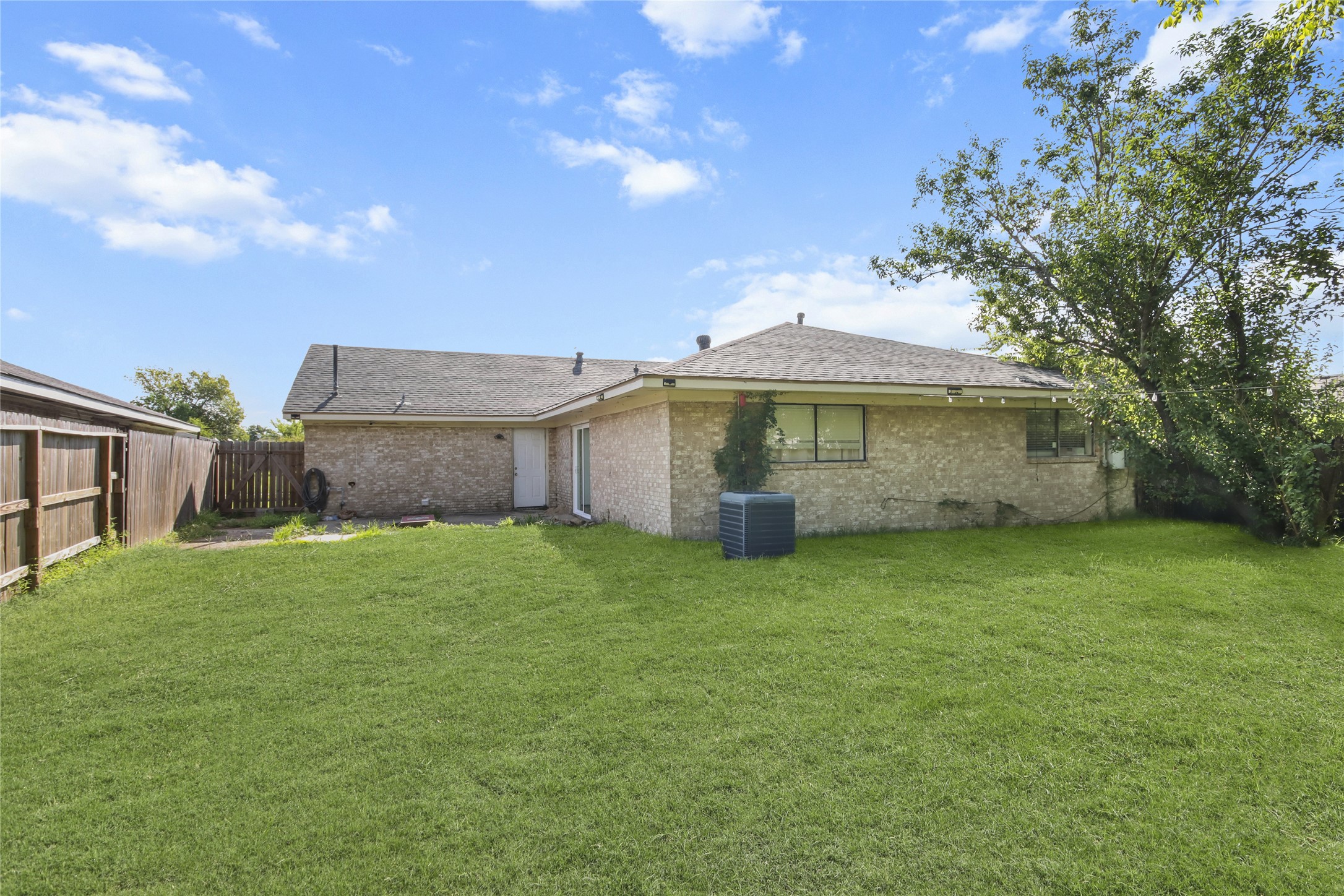 The spacious backyard offers plenty of green space and a wood privacy fence, with string lighting for evening ambiance. Both the back door and sliding glass door provide easy access between the home and the spacious backyard.