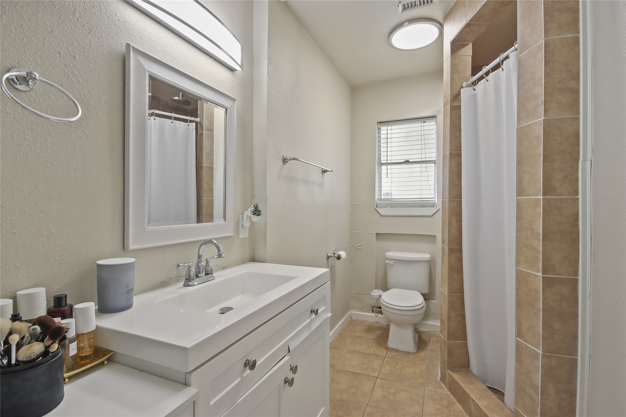 The primary bathroom features a tiled walk-in shower with a rainfall showerhead, a wide vanity with generous counter space, and a window that brings in natural light.