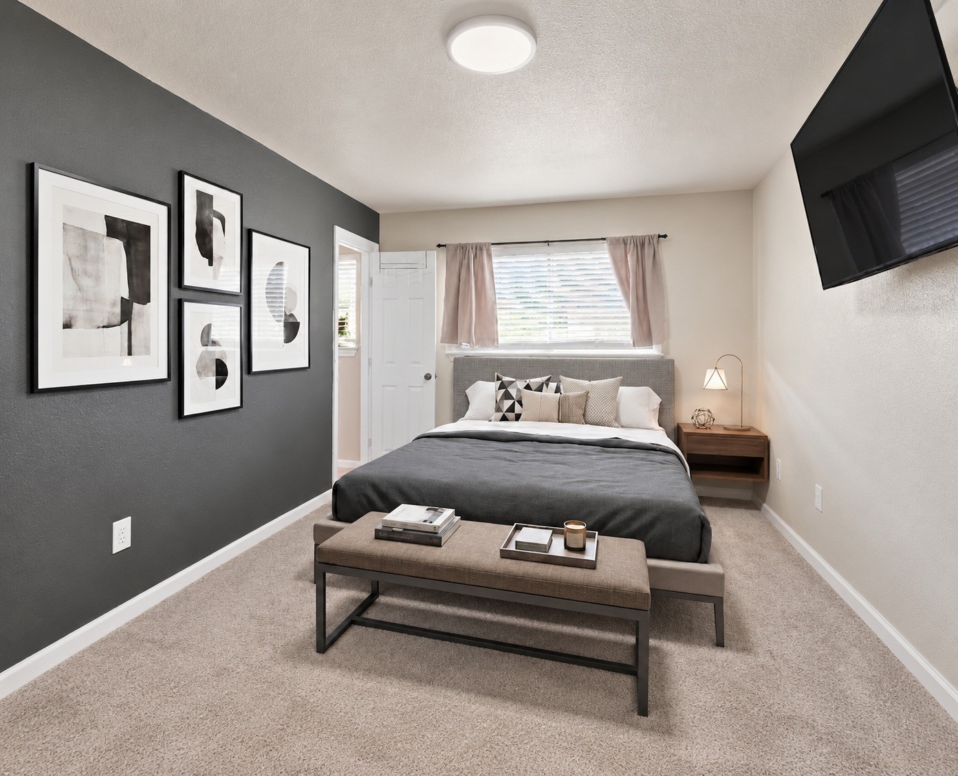 The primary bedroom offers a bold accent wall, plush carpet, and a large window for natural light. Virtually staged.