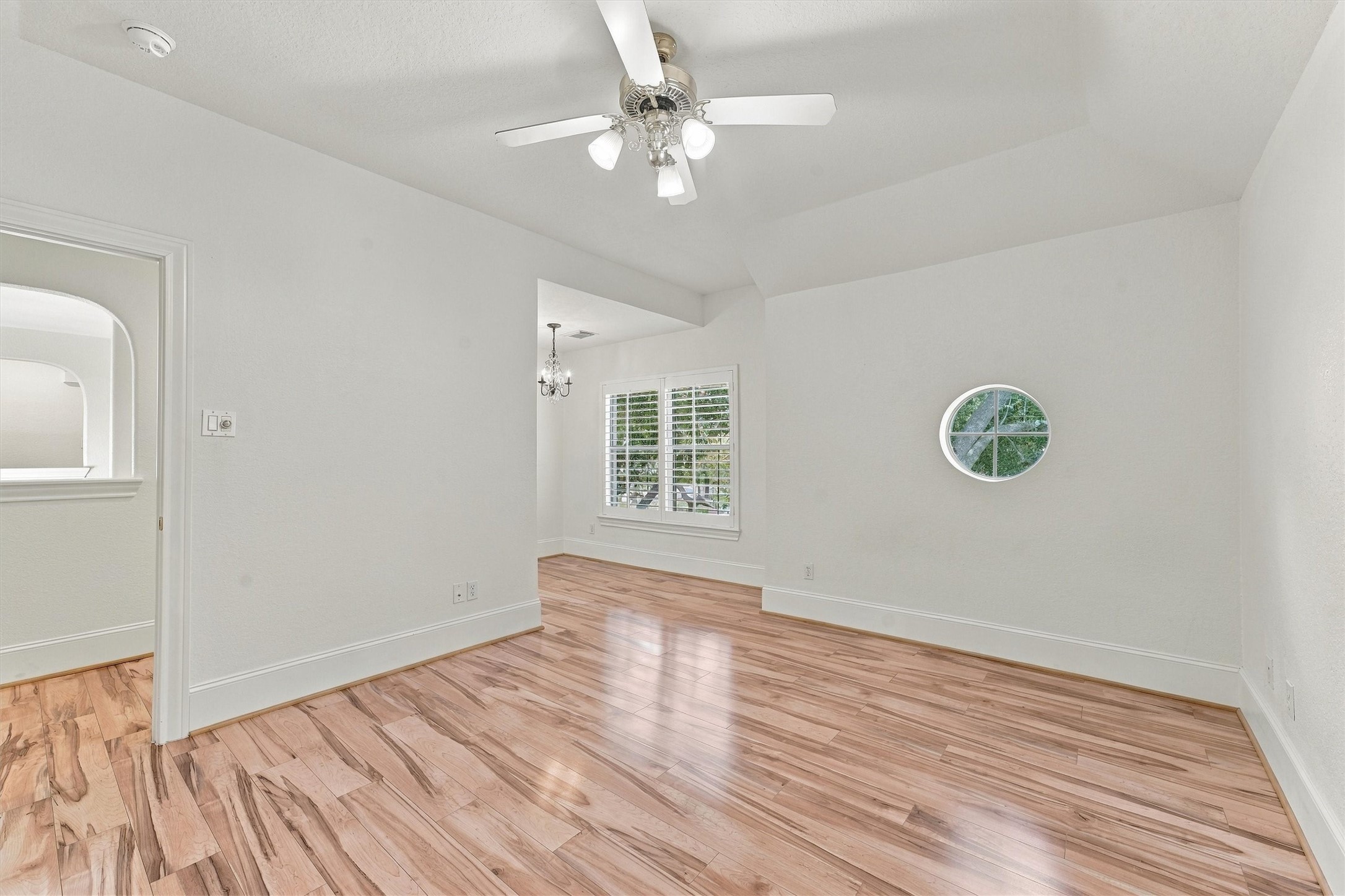 Bedroom three - Upstairs bedroom with sitting area, ceiling fan, wood flooring, round accent window, and chandelier with plantation shutters.