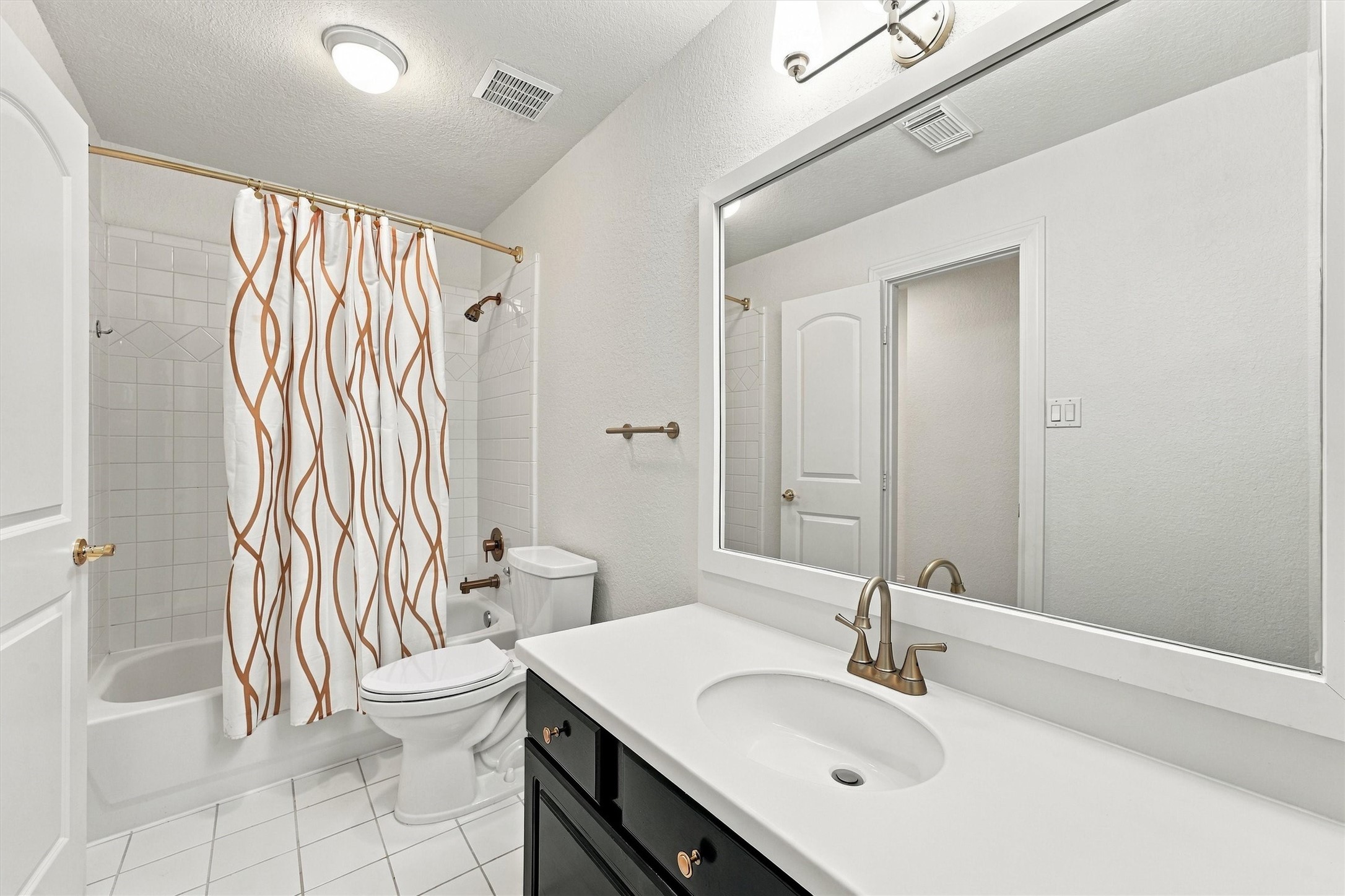 Second floor - Second Bathroom with black vanity, large framed mirror, brass fixtures, white tile floor, and a tub and shower combination with tile surround.