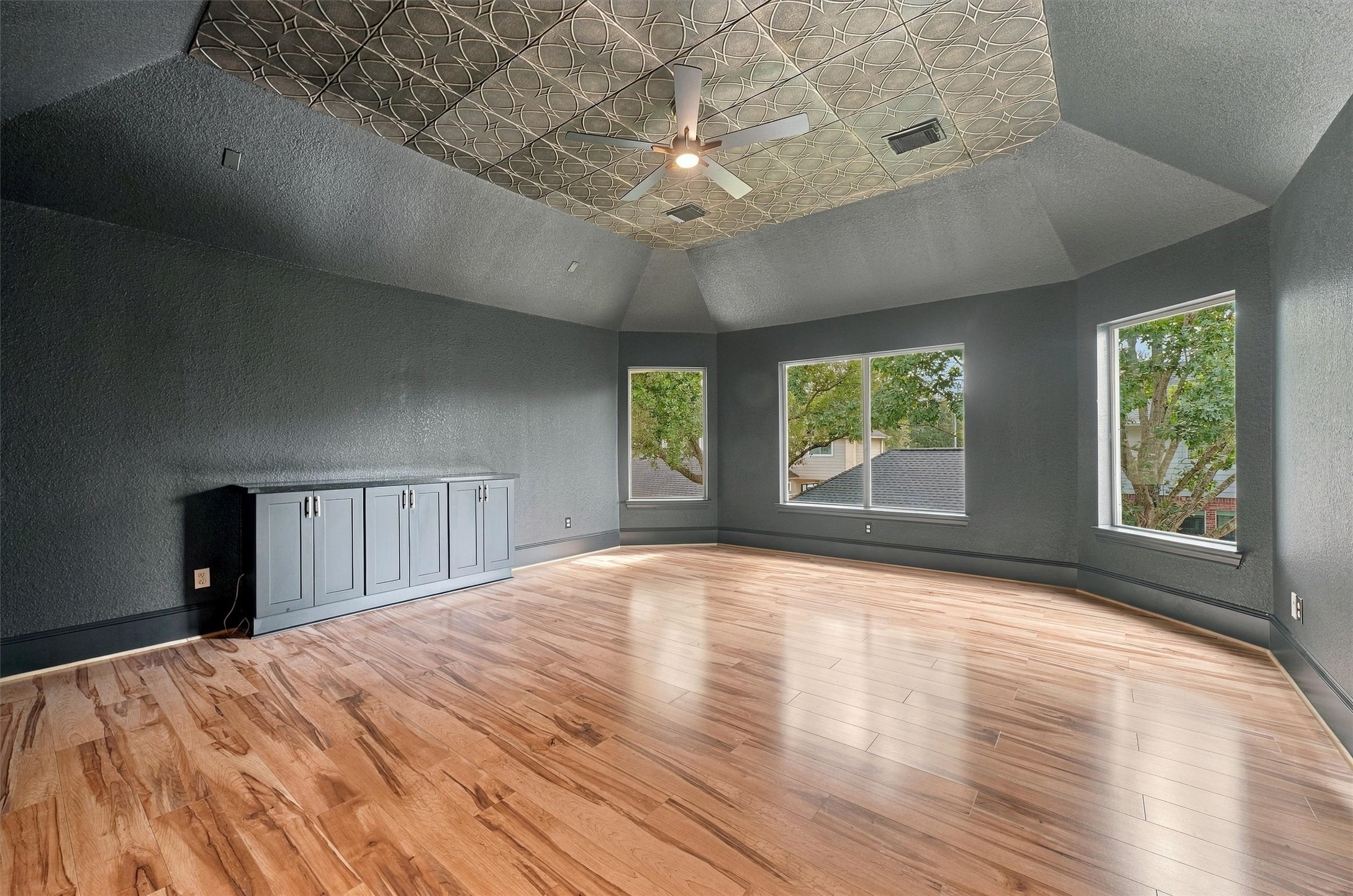 Media room or extra room located upstairs with decorative ceiling, ceiling fan, built-in cabinets, wood flooring, and large windows overlooking the treetops.