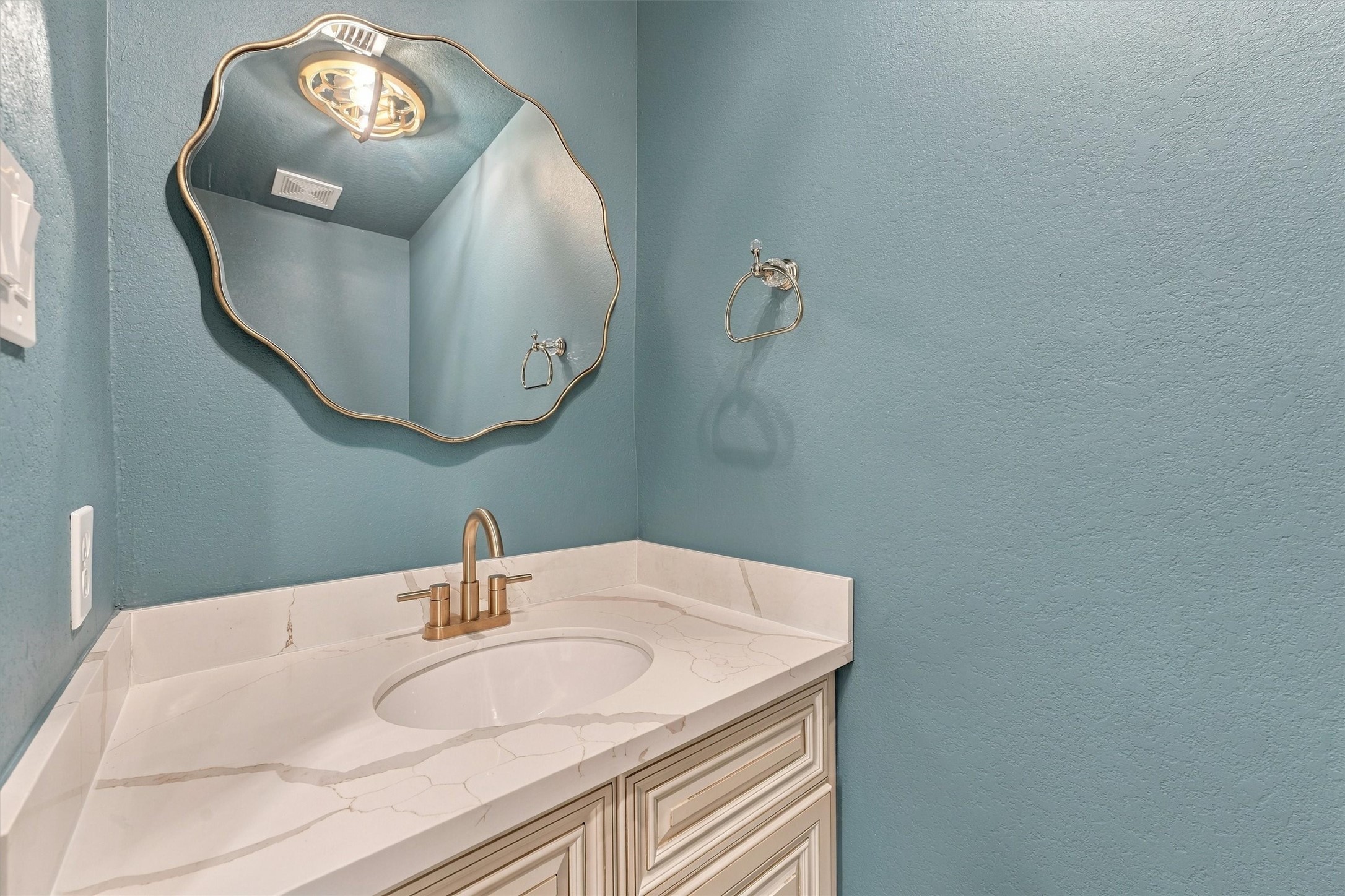 Downstairs half bath with teal walls, decorative mirror, and vanity.