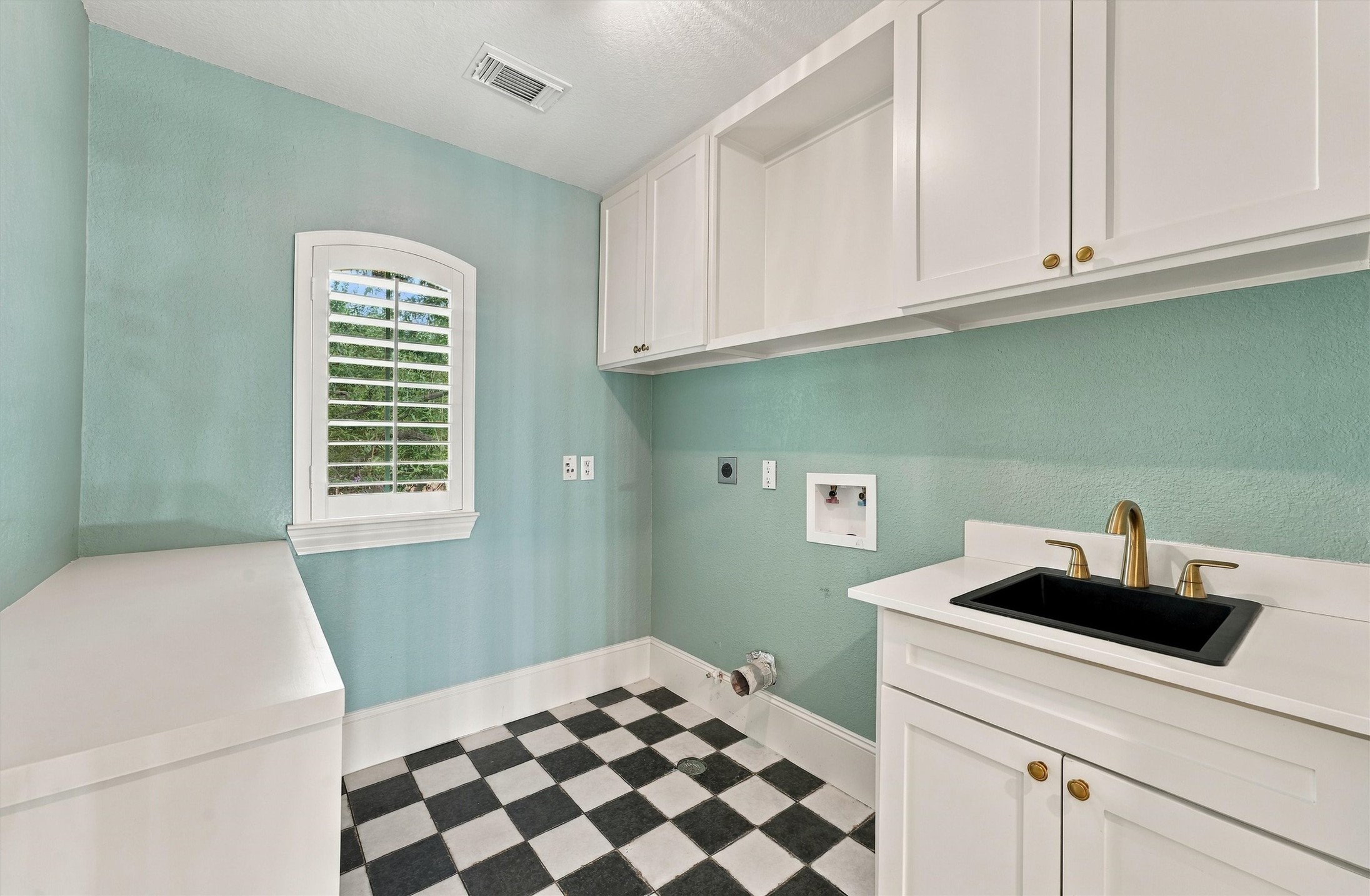 Second-floor laundry room with aqua walls, checkerboard floor, white cabinets, utility sink, and plantation shutters.