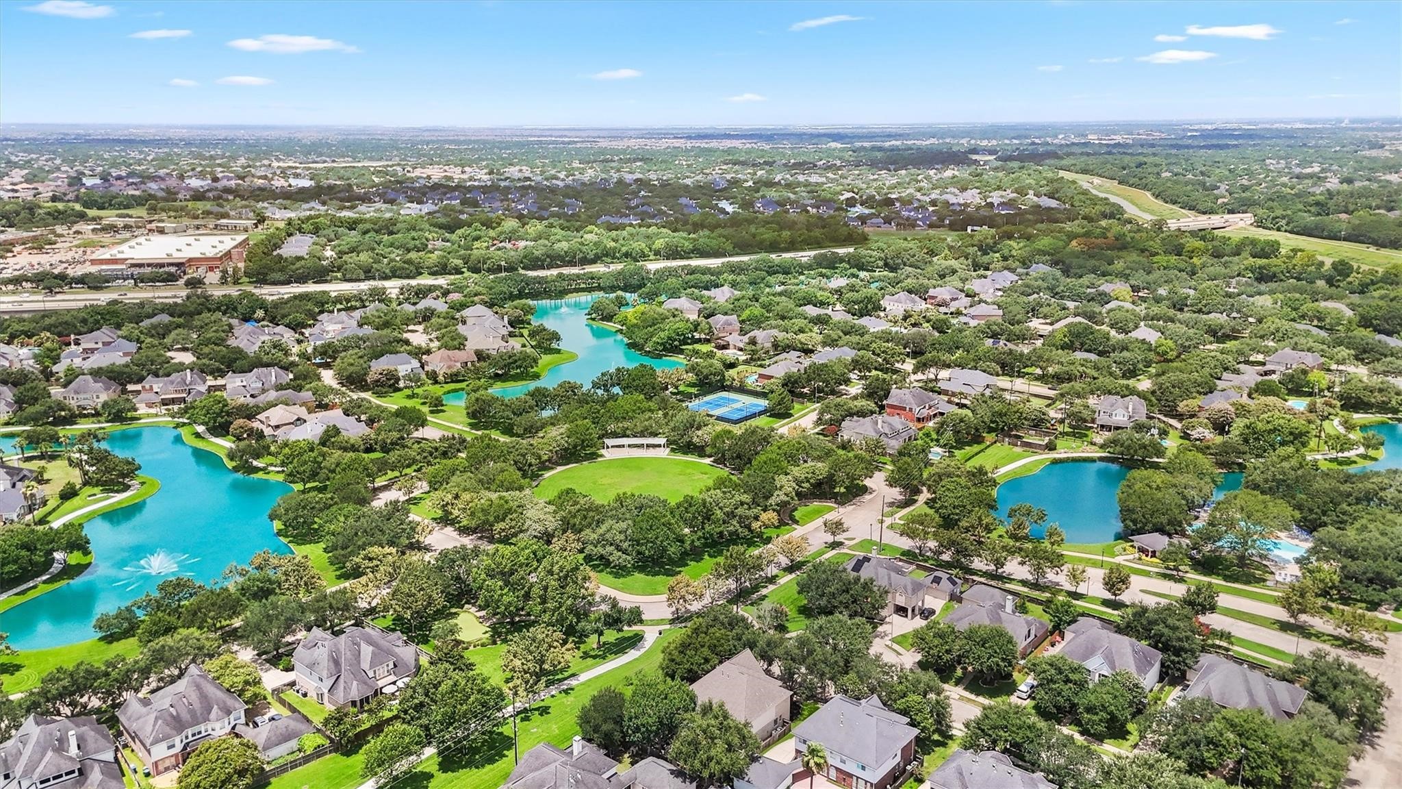 This aerial photo showcases a pictures que Grand Lakes neighborhood with lush greenery, winding streets, and houses nestled around serene blue lakes. The area features ample green space and a community pool.