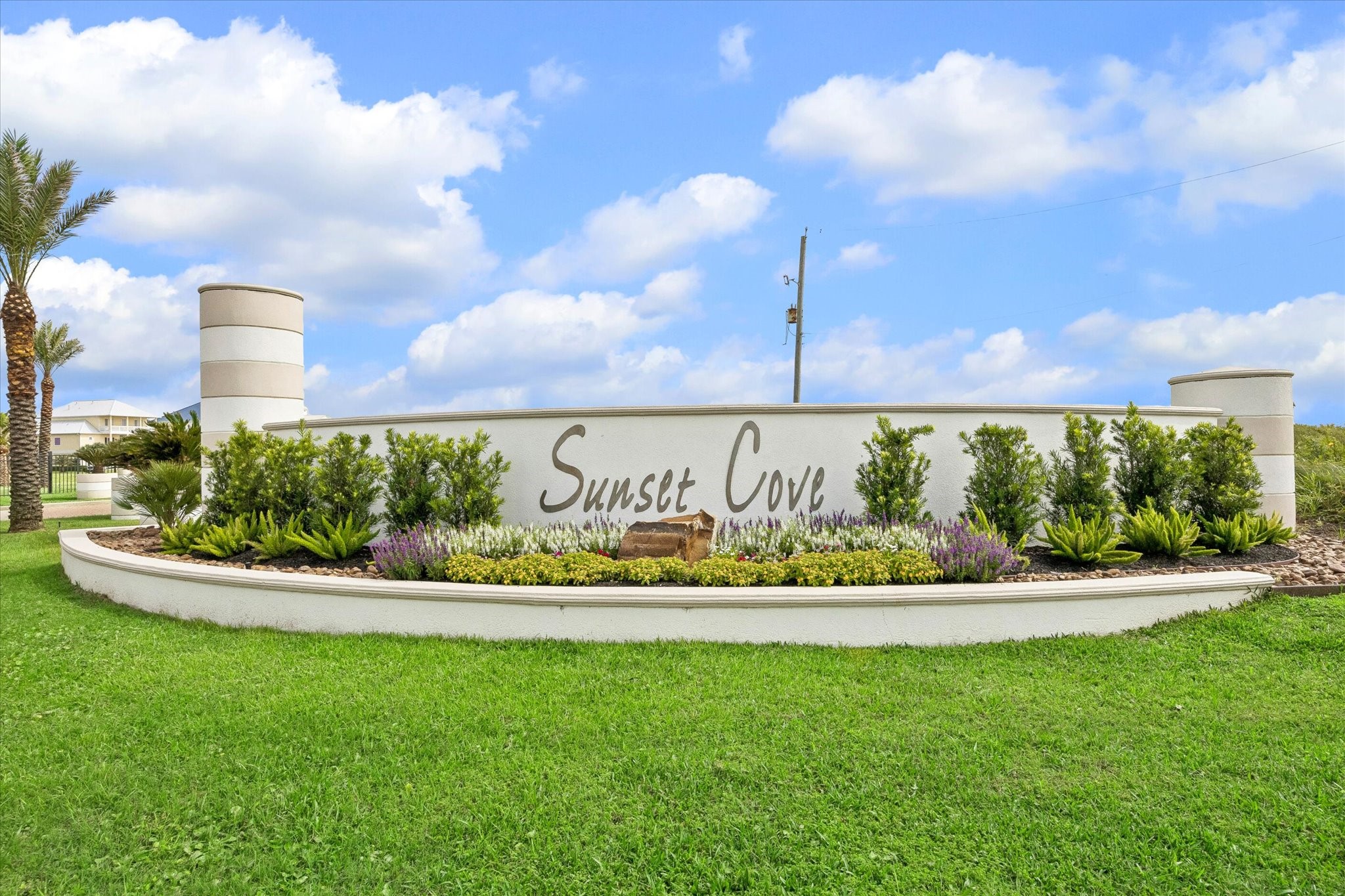 Landscaped Sunset Cove signage gives the neighborhood a polished coastal entrance, with palms and layered plantings adding to the arrival. A clean first impression for a gated community built around beachside and bayside living.