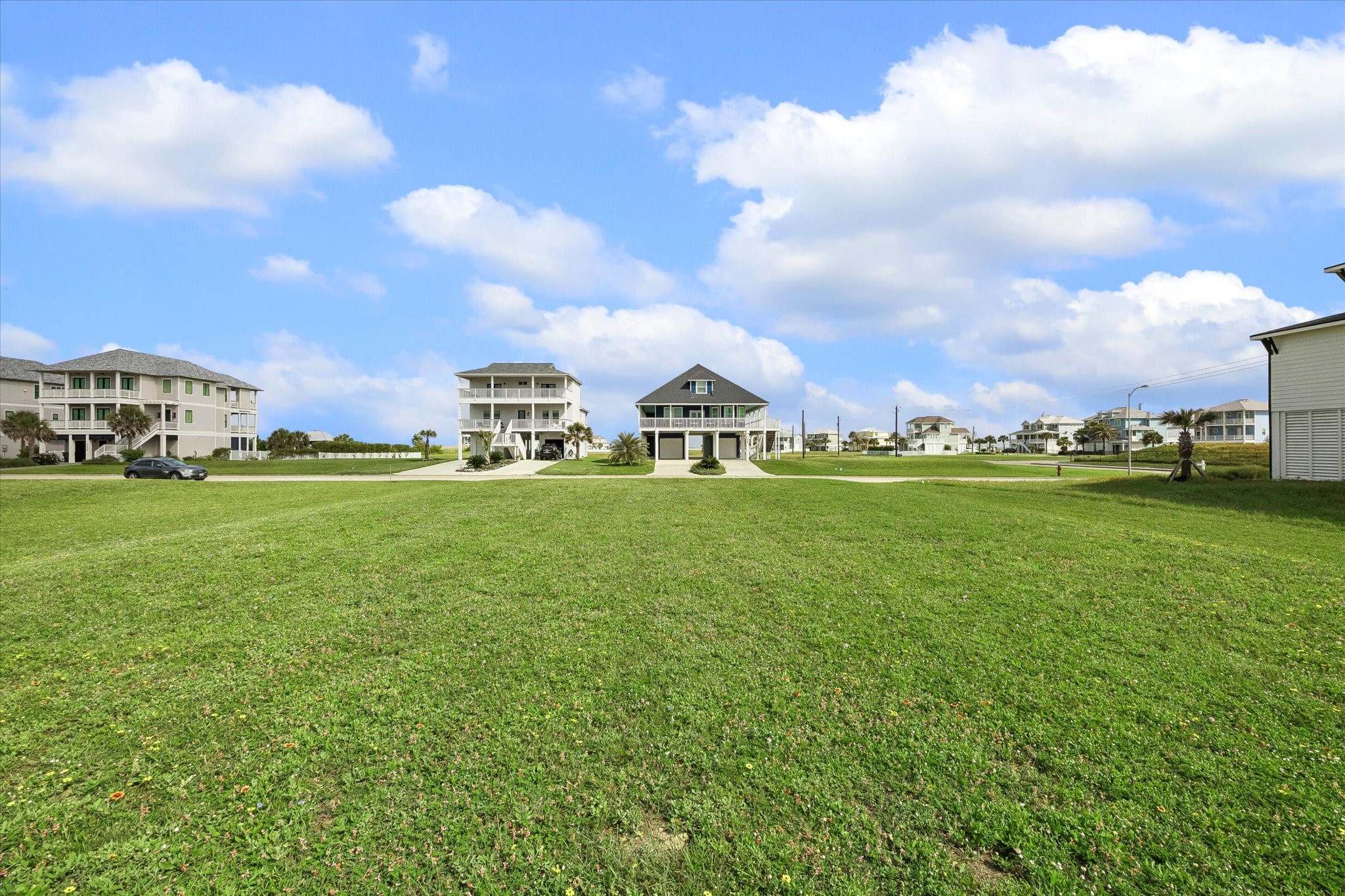 Wide open green space surrounds the homesite, with neighboring coastal homes giving a clear sense of the setting and scale. A peaceful spot to plan a beach-area build with room to take in the sky, breeze, and neighborhood views.