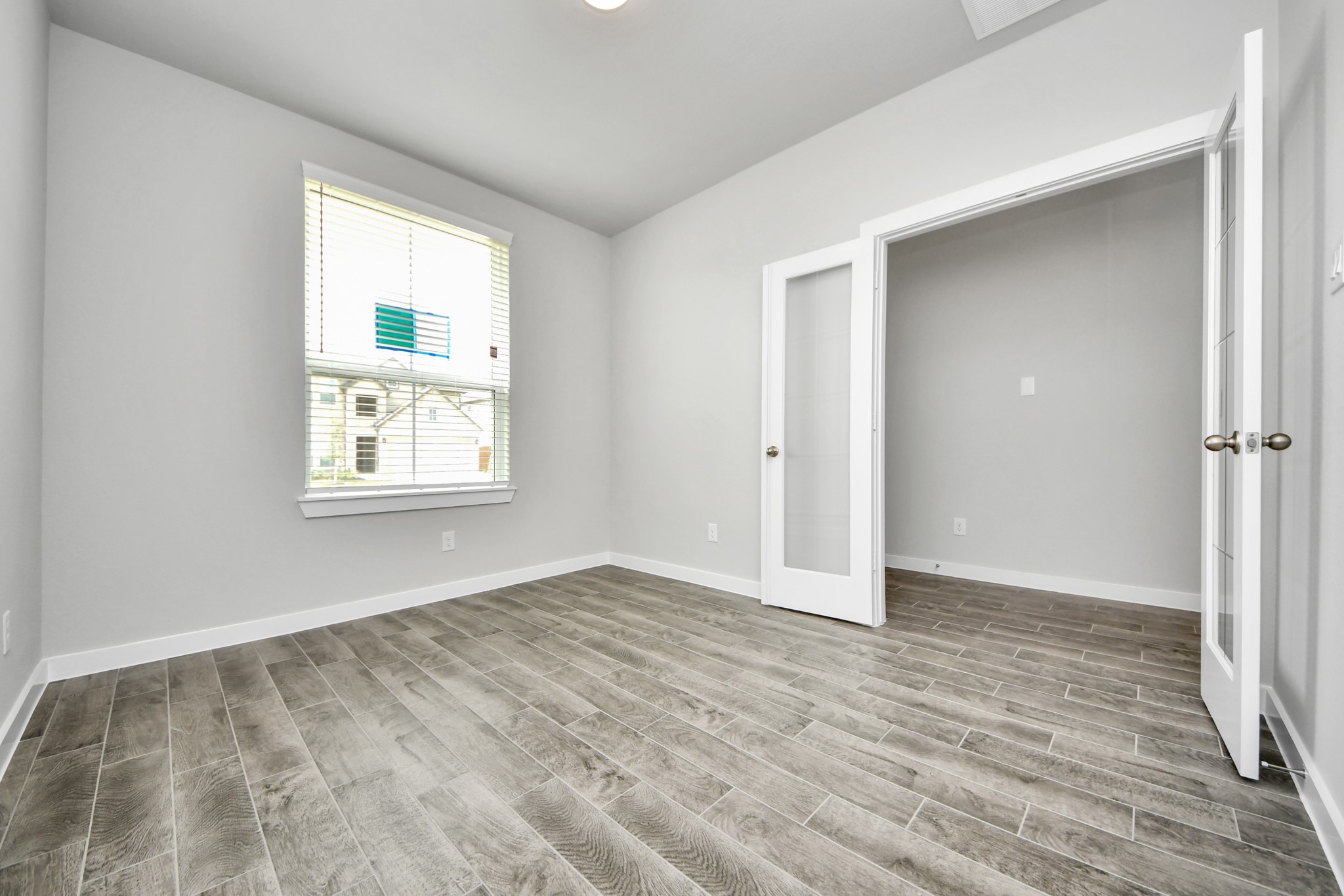 Experience the perfect blend of sophistication and warmth in this home office, boasting elegant wood-look tile flooring and flooded with natural light from expansive windows and French doors. Sample photo of completed home with similar floor plan. Actual colors and selections may vary.