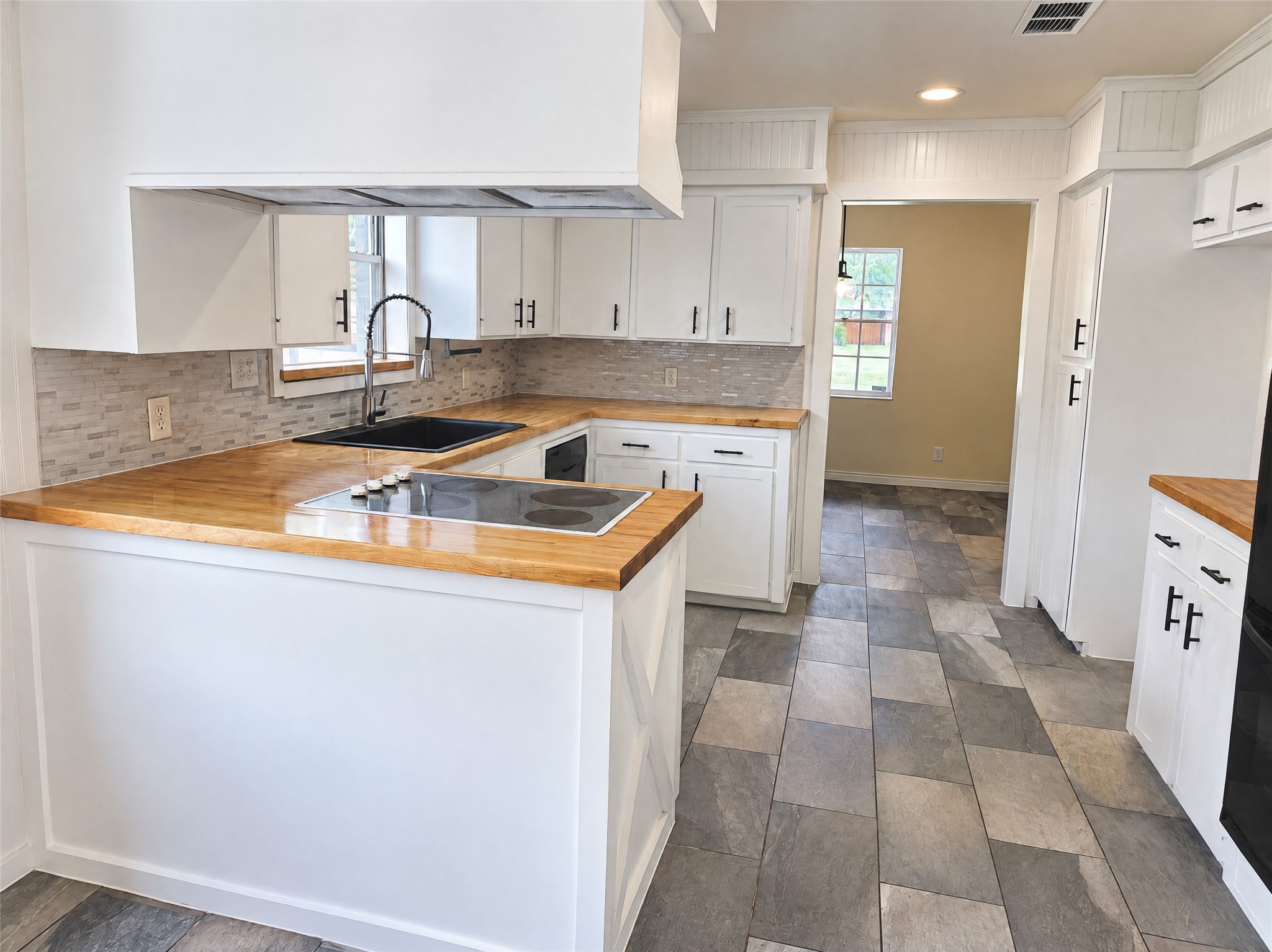 Complete with an integrated cooktop, undermount black composite sink, stainless gooseneck faucet, dishwasher, and charming beadboard detailing, meal prep is an absolute pleasure.