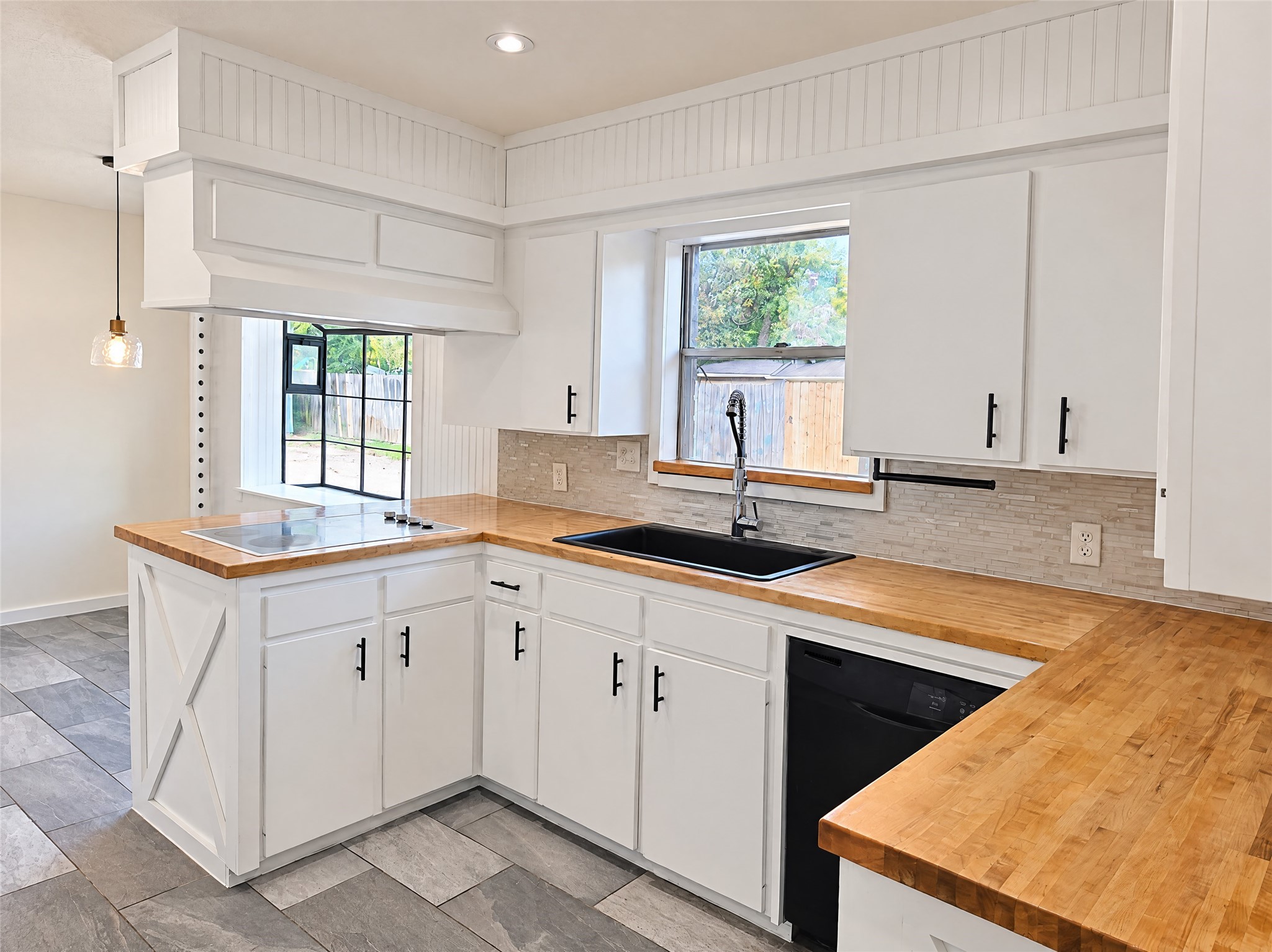 Crisp white cabinetry with modern matte black pulls pairs beautifully with solid butcher block counters and a textured tile backsplash.