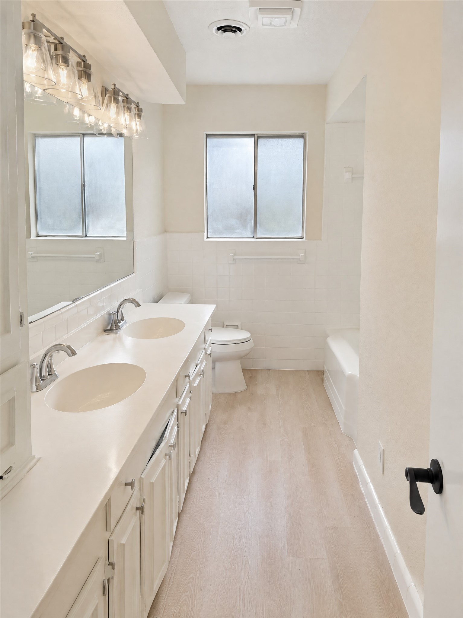 Serving the secondary bedrooms and guests, this full bathroom features an expansive double vanity, framed vanity lighting with vintage-inspired glass shades, pristine white tile surround, and a tub/shower combination.