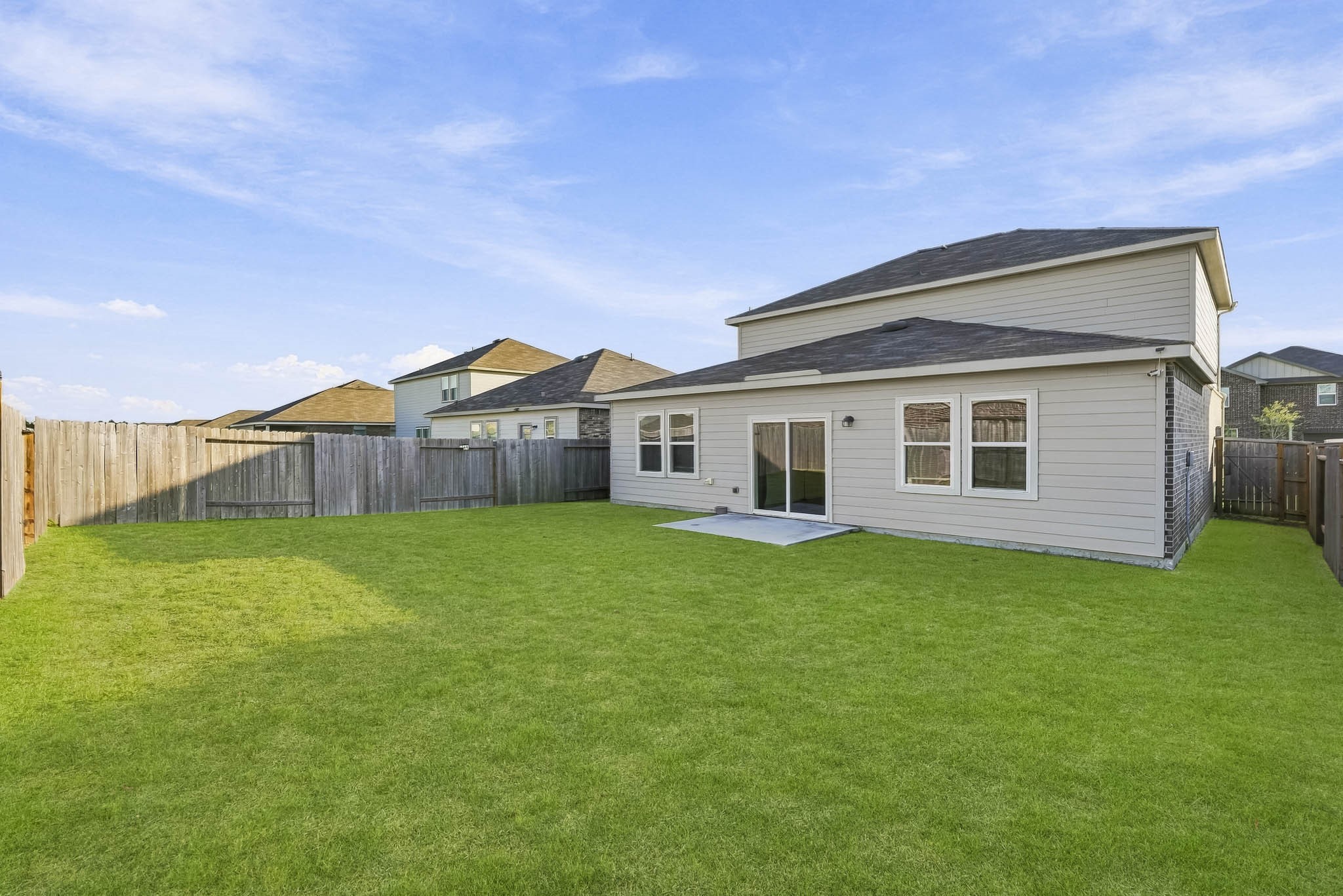 This spacious backyard offers an expansive stretch of lush green lawn, creating an inviting outdoor retreat with endless possibilities for relaxation, recreation, and entertaining. Fully enclosed by wooden privacy fencing, the yard provides a comfortable setting for outdoor activities. A concrete patio sits just outside the sliding glass doors, offering a convenient space for outdoor seating or grilling.