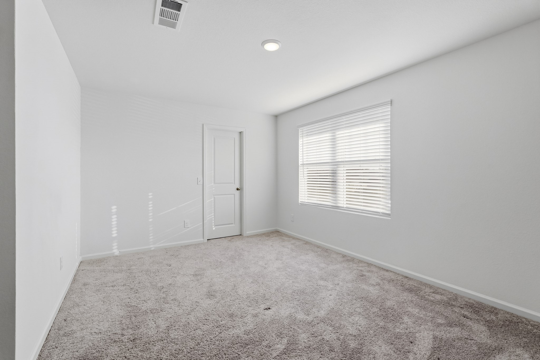 This bright and inviting secondary bedroom features a comfortable, spacious layout with crisp white walls, plush neutral carpeting, and a clean, contemporary aesthetic.