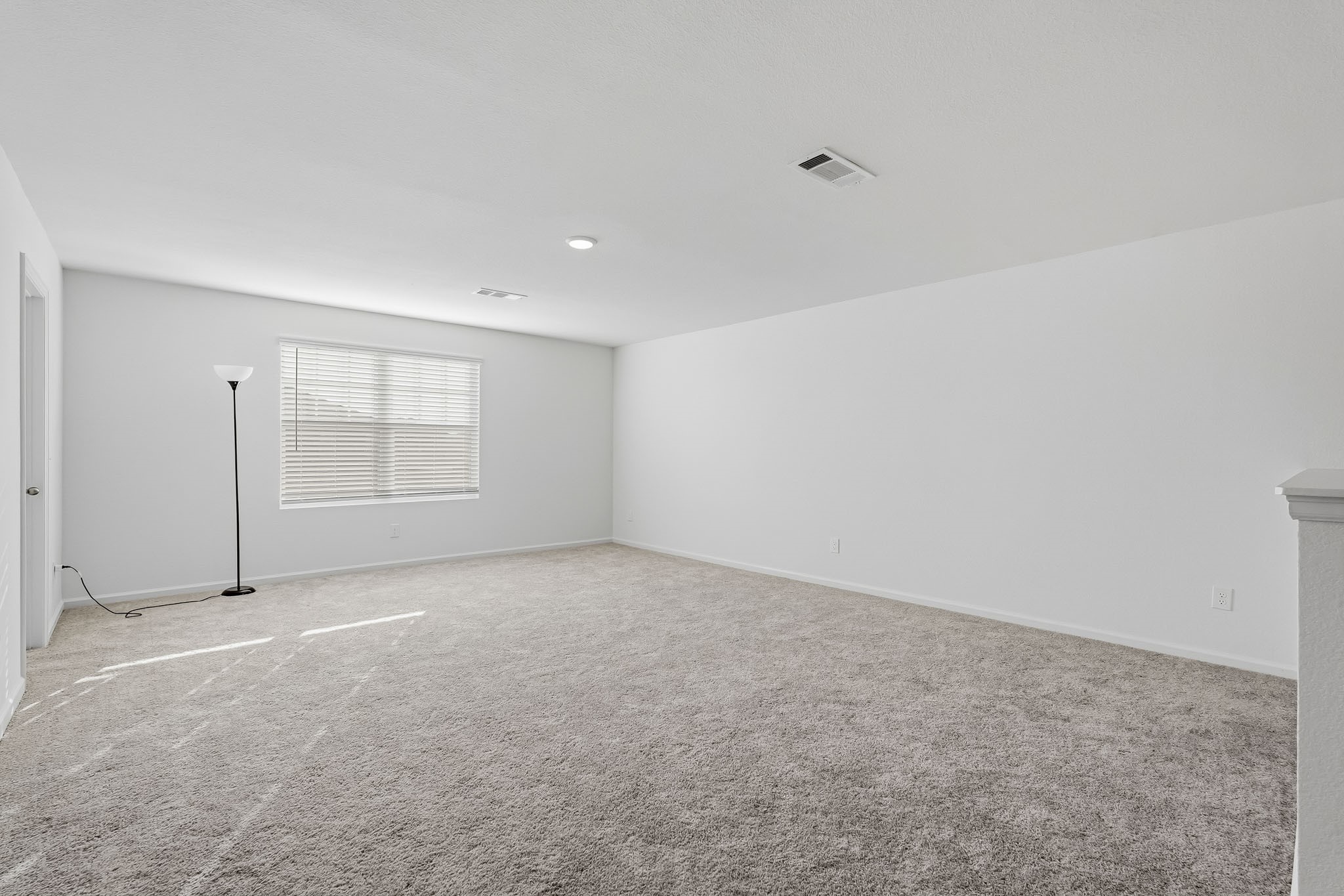 This expansive upstairs game room offers an incredible flexible living space, perfect for entertainment, recreation, or everyday relaxation. Featuring a spacious open layout, plush neutral carpeting, crisp white walls, and recessed ceiling lighting, the room provides a bright and welcoming atmosphere. A large window with adjustable blinds allows natural light to fill the space, enhancing its airy feel.