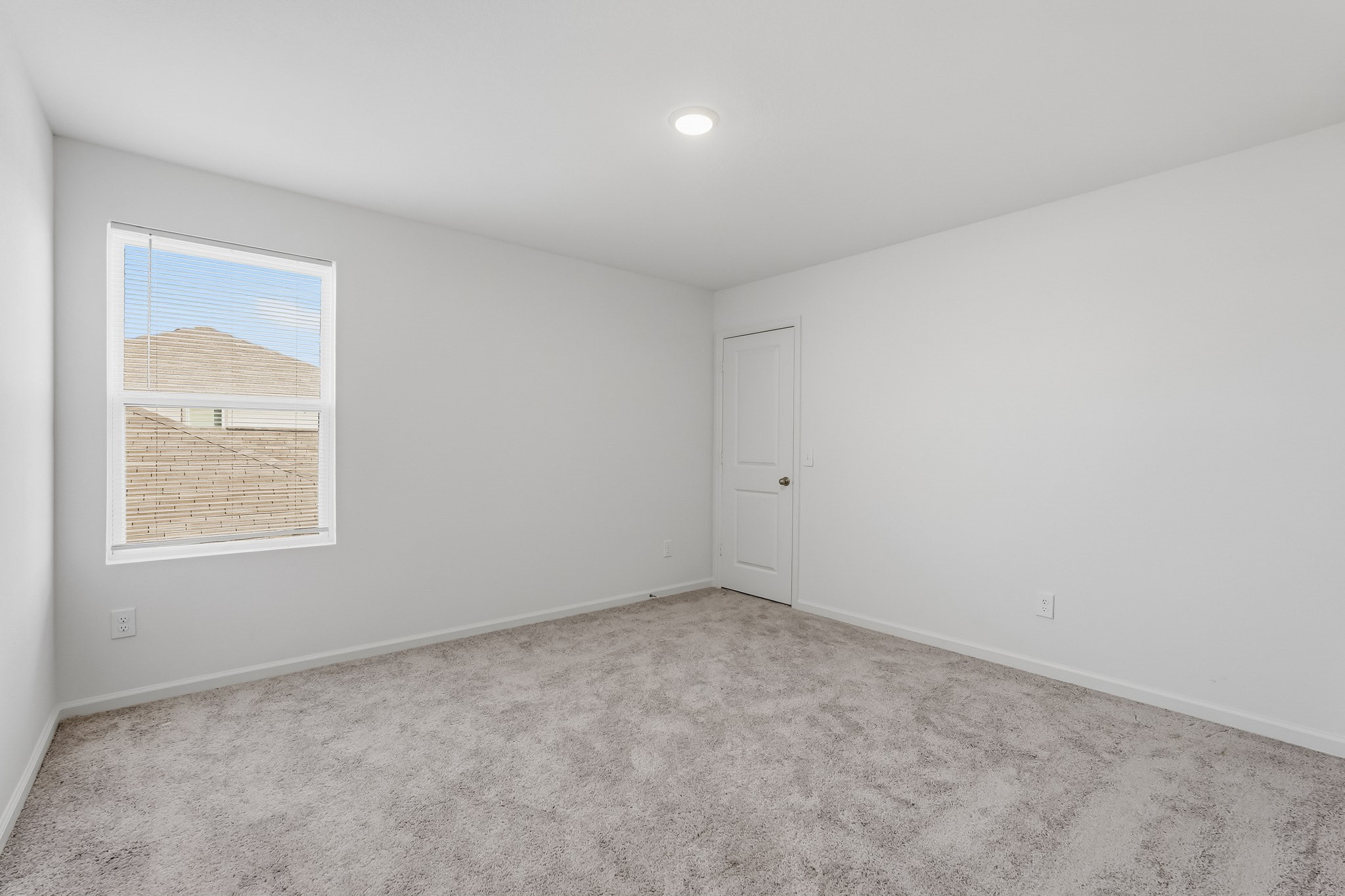 This bright and spacious secondary bedroom features a clean, modern design with crisp white walls, plush neutral carpeting, and a generous layout. A convenient closet with a classic paneled door adds practical storage, completing this comfortable and functional space.