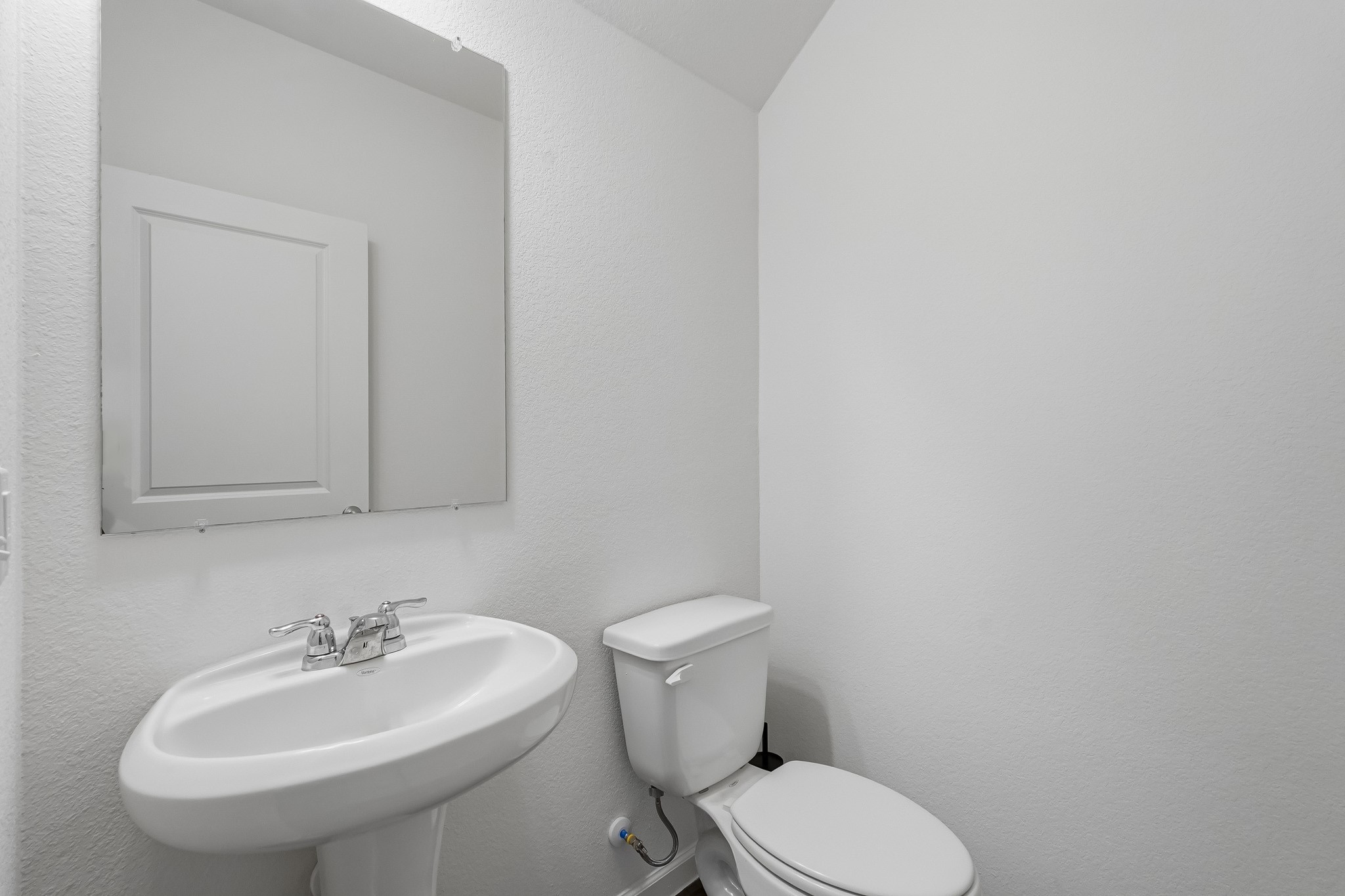 This compact half bathroom features a clean, minimalist design with crisp white textured walls and a bright, neutral color palette.