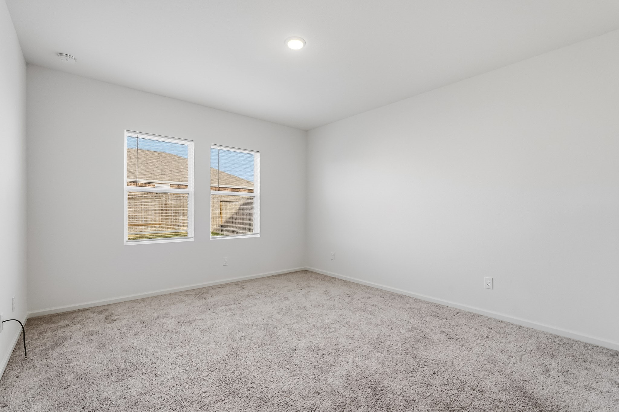 This spacious master bedroom features a bright, open layout with crisp white walls, soft neutral carpeting, and a clean, modern aesthetic. Two generously sized windows allow natural light to fill the room, creating an airy and welcoming atmosphere. The high ceiling and recessed lighting enhance the sense of openness, while the expansive floor space offers flexibility for a variety of bedroom arrangements.