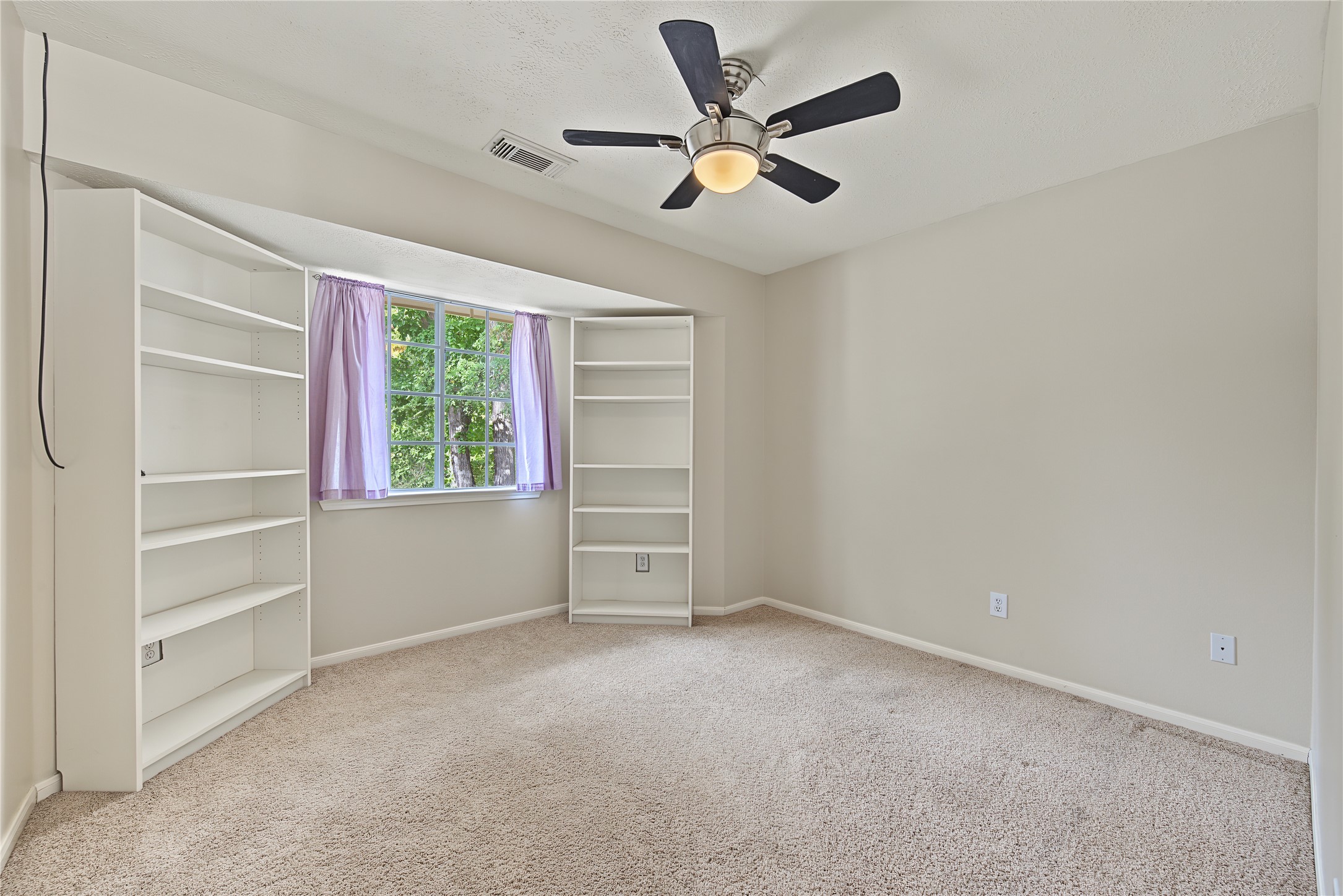 Secondary Bedroom 1 with a ceiling fan, natural light, and shelving on both sides of the window