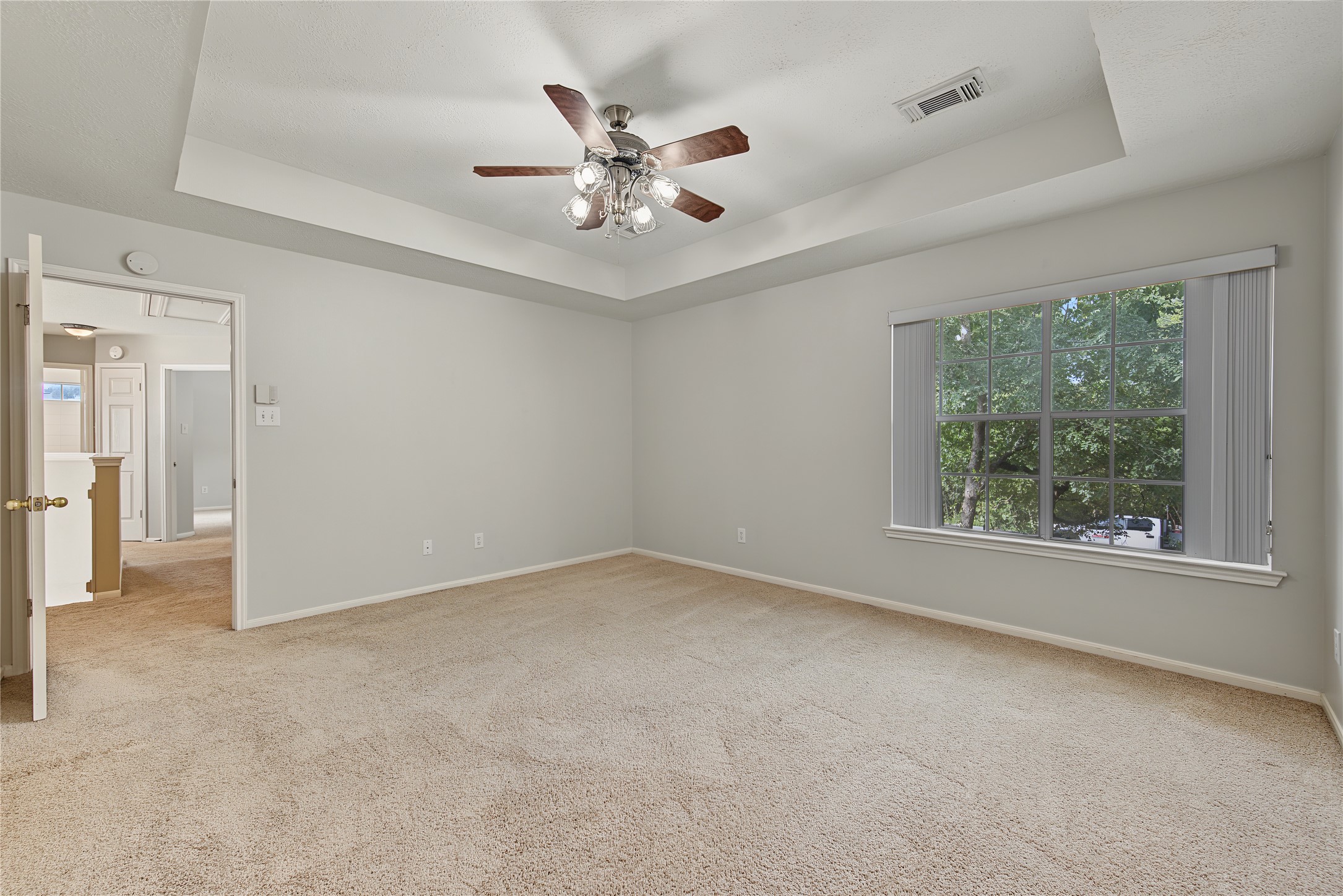 A lovely, generously sized primary suite with a tray ceiling, ceiling fan, and backyard view