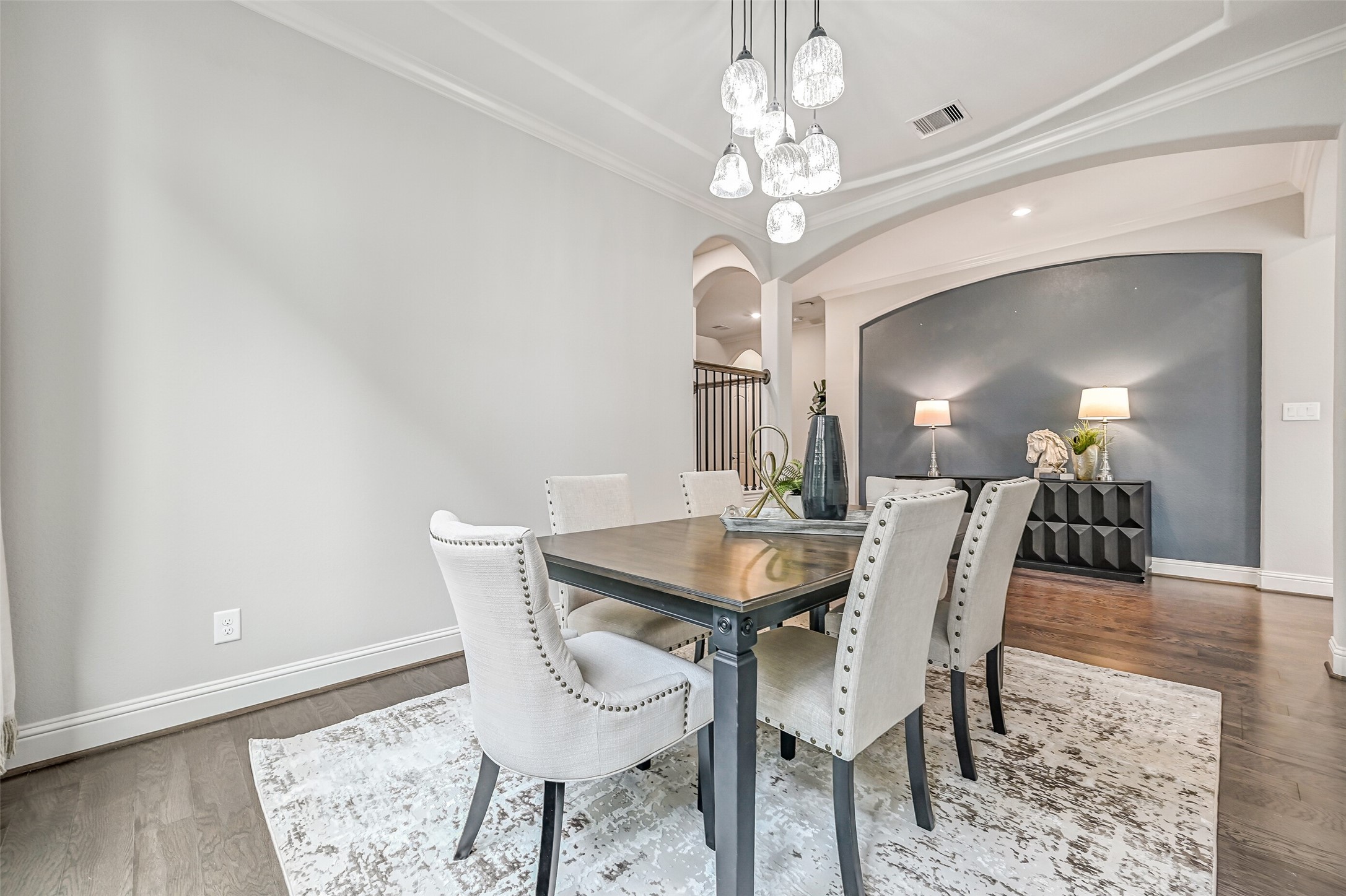 Another look at the dining room reveals its attractive architectural details, including the arched opening, decorative ceiling trim & striking light fixture. The adjoining hallway features a deep blue-gray accent wall that adds a beautiful contrast to the home's neutral palette.