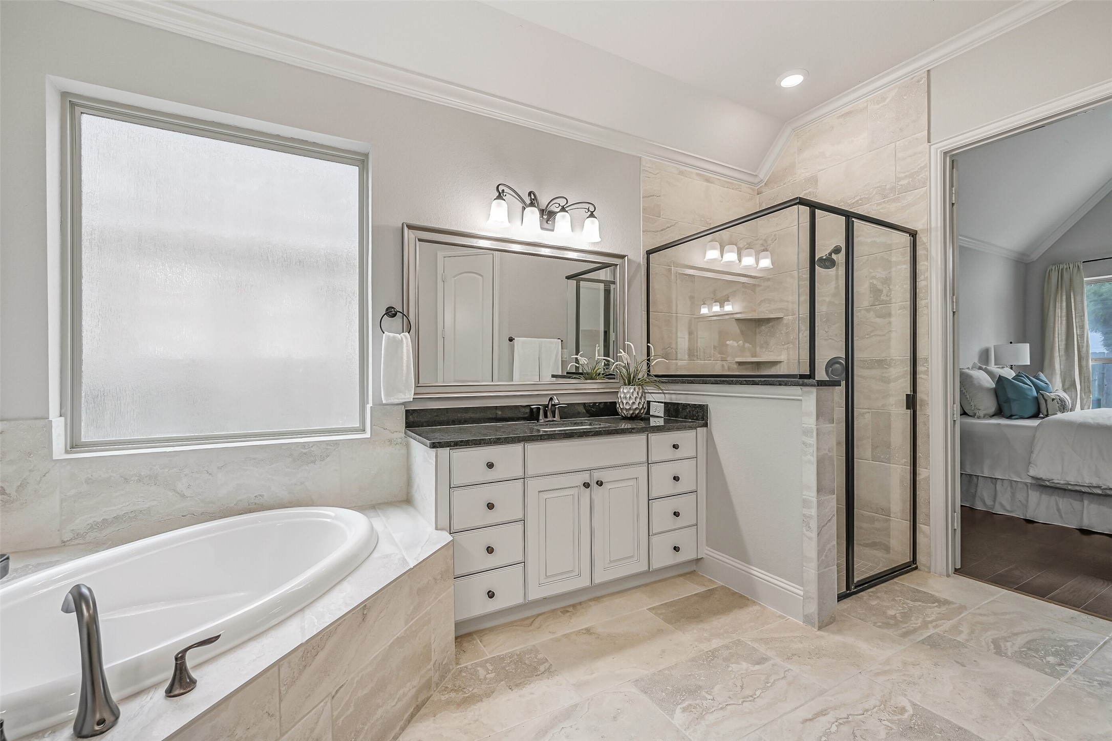 Just off the primary bedroom, the generously sized bathroom features a corner soaking tub beneath a large privacy-glass window, separate glass-enclosed shower with tiled surround & two individual granite-topped vanities. Coordinating stone-look tile flooring ties everything together.
