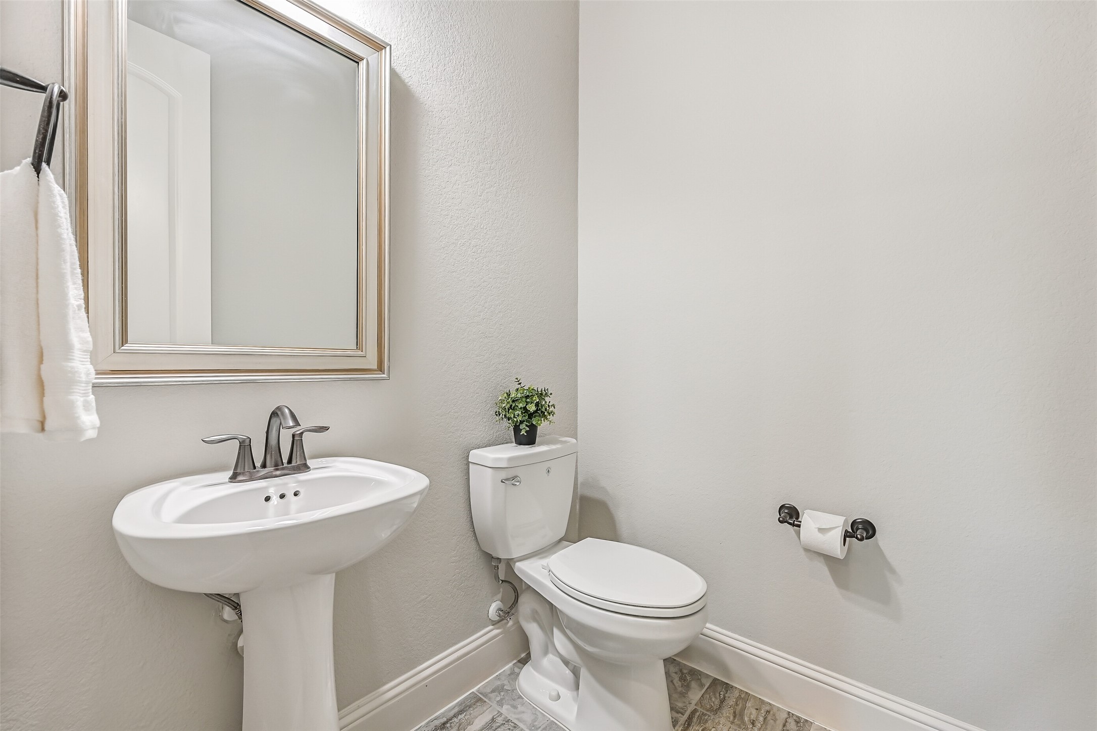 Just off the foyer, near the garage entrance and staircase, you'll find a convenient half bath with a pedestal sink, framed mirror & stone-look tile flooring.