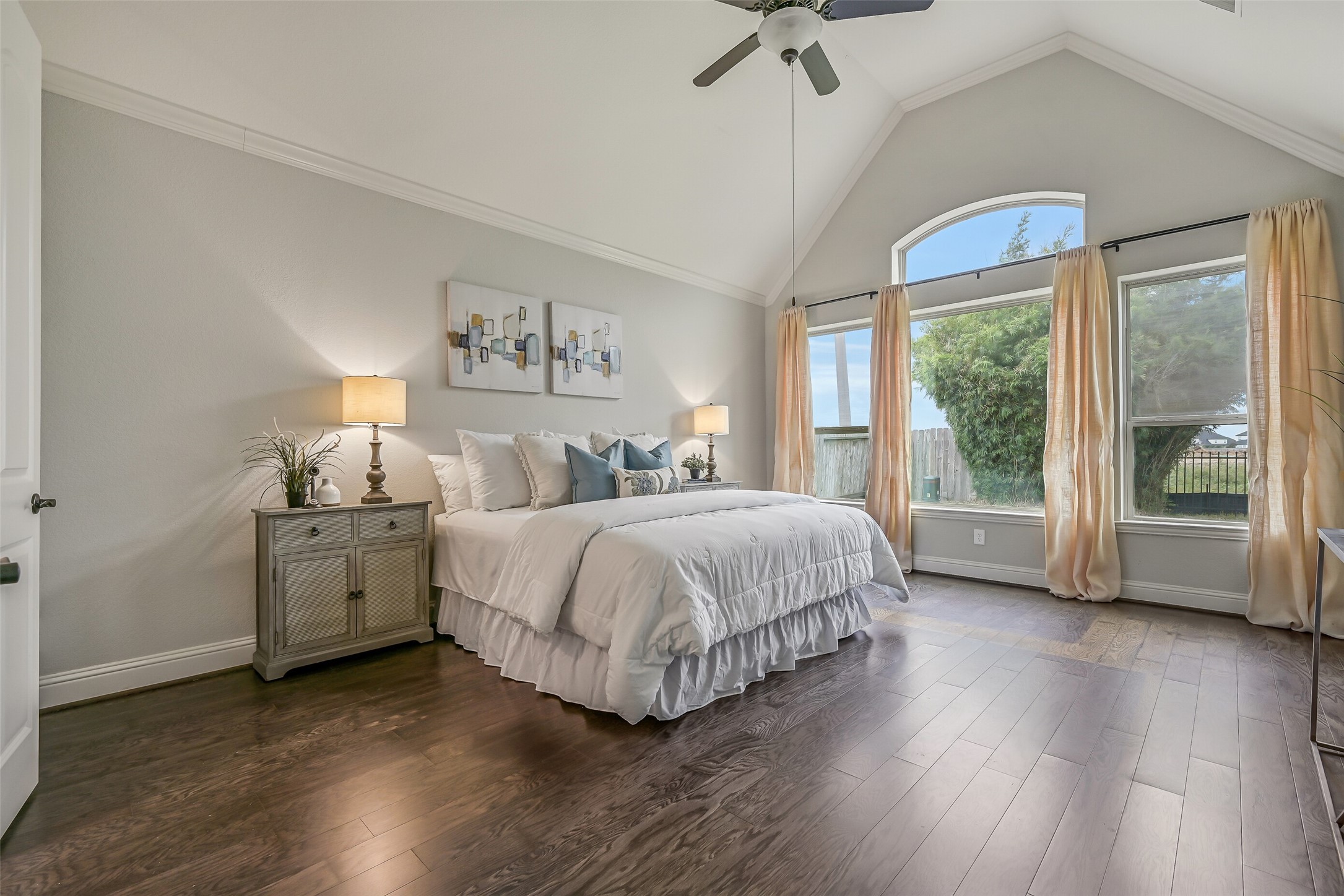The spacious first-floor primary suite feels especially inviting with its dramatic 14' vaulted ceiling, rich luxury vinyl plank flooring & beautiful arrangement of rear-facing windows topped by an arched transom. Crown molding & a lighted ceiling fan add the finishing touches.