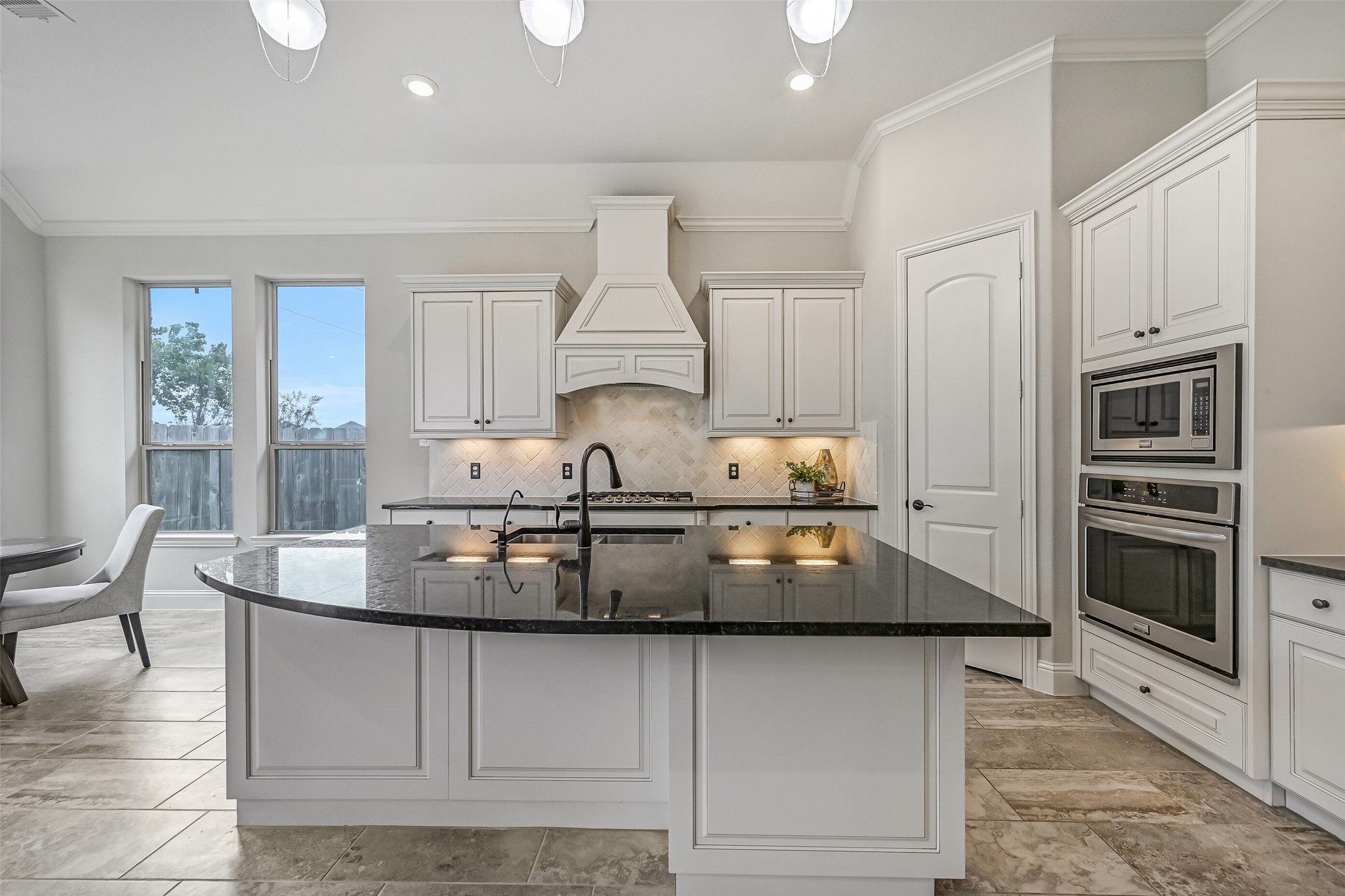 The oversized granite island is the centerpiece of this beautiful kitchen, offering plenty of prep space, seating & additional cabinetry. Crisp white cabinetry, custom pendant lighting, a decorative vent hood & built-in stainless appliances create a polished, coordinated look.