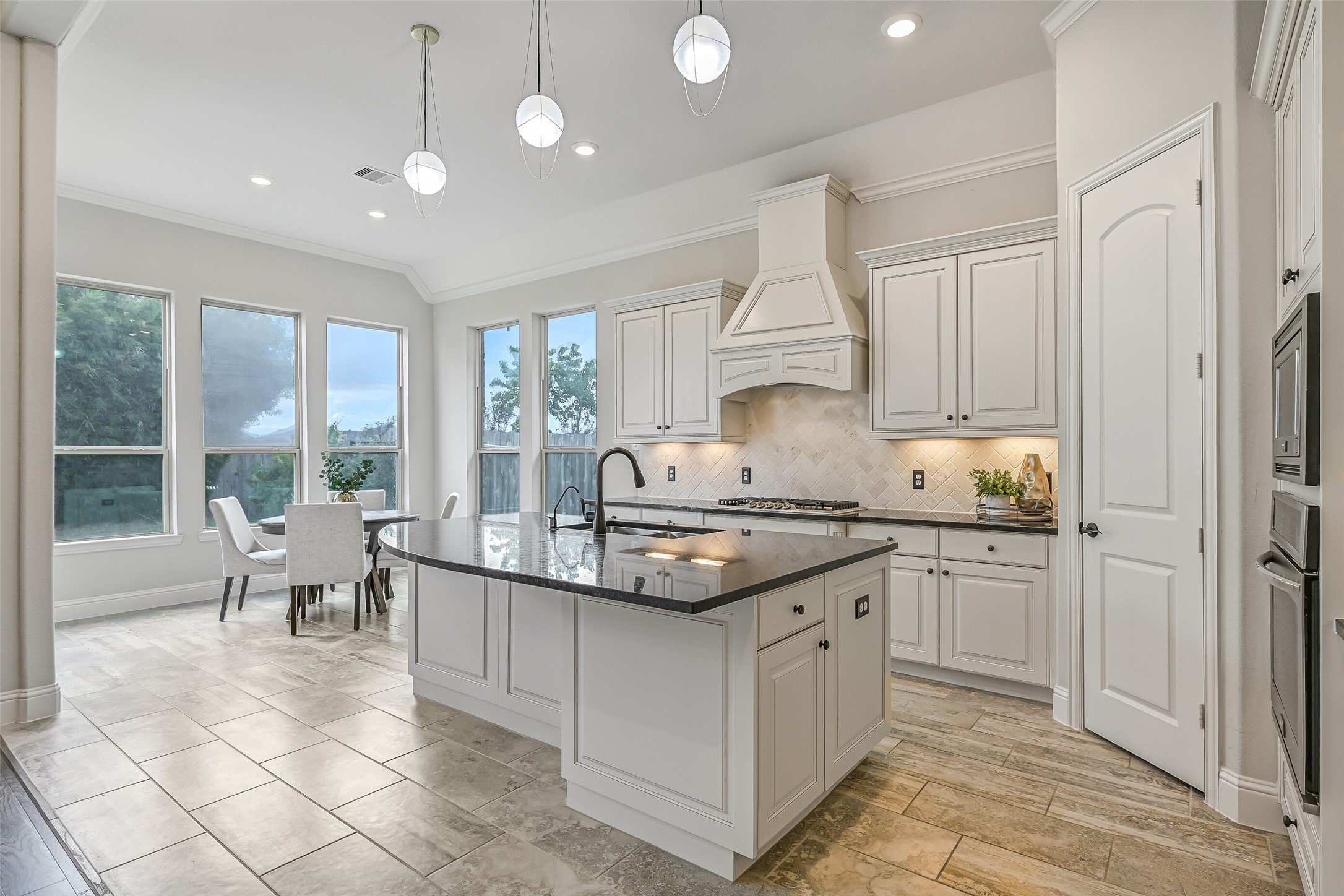 From the kitchen, enjoy a lovely view into the sunlit breakfast room! The 5-burner Frigidaire gas cooktop sits beneath a custom vent hood, framed by a herringbone brick backsplash, granite countertops & undercabinet task lighting.
